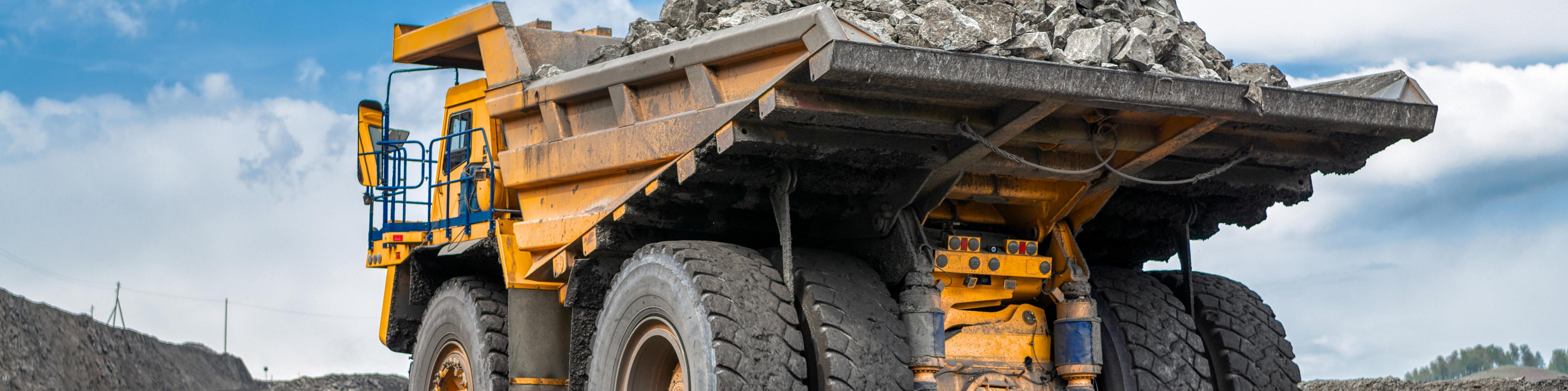 Rock transportation by dump trucks. Large quarry yellow truck. Transport industry. Mining truck is driving along a mountain road.