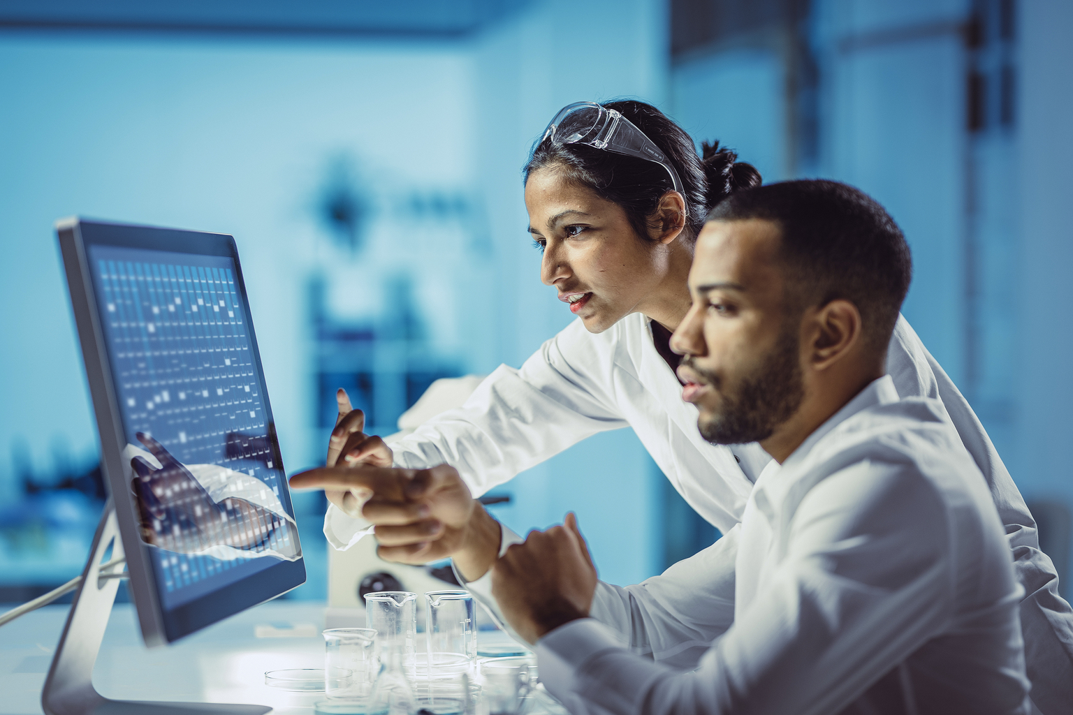 Two chemist in lab coat analyzing on a touch screen computer