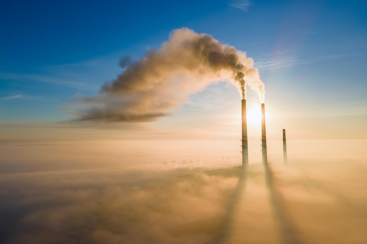 Aerial view of coal power plant high pipes with black smoke moving up polluting atmosphere at sunset.