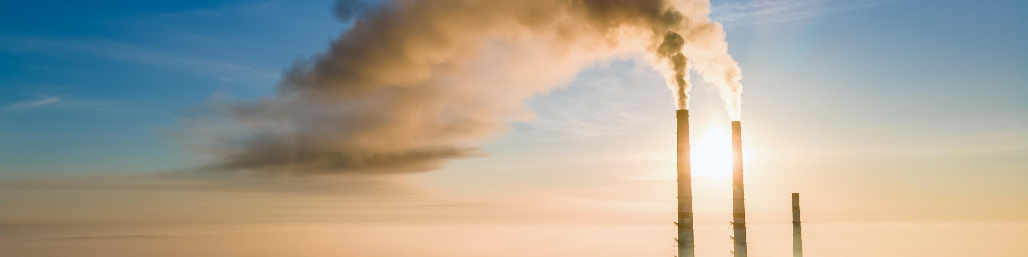 Aerial view of coal power plant high pipes with black smoke moving up polluting atmosphere at sunset.