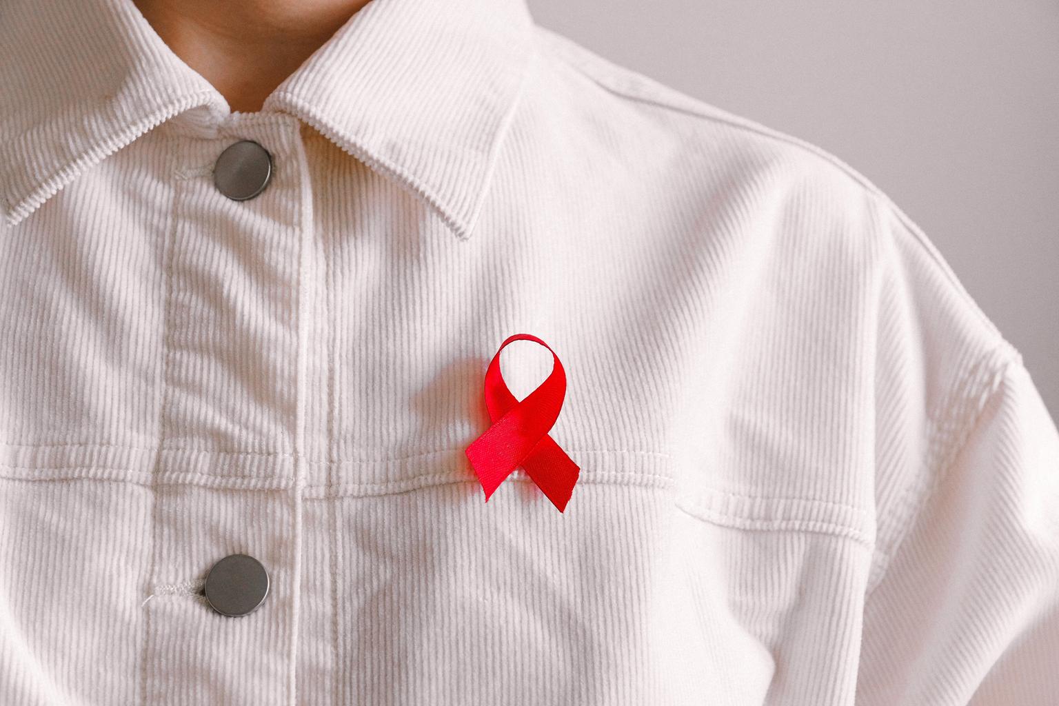 Person wearing white corduroy shirt with red HIV/AIDS ribbon displayed prominently