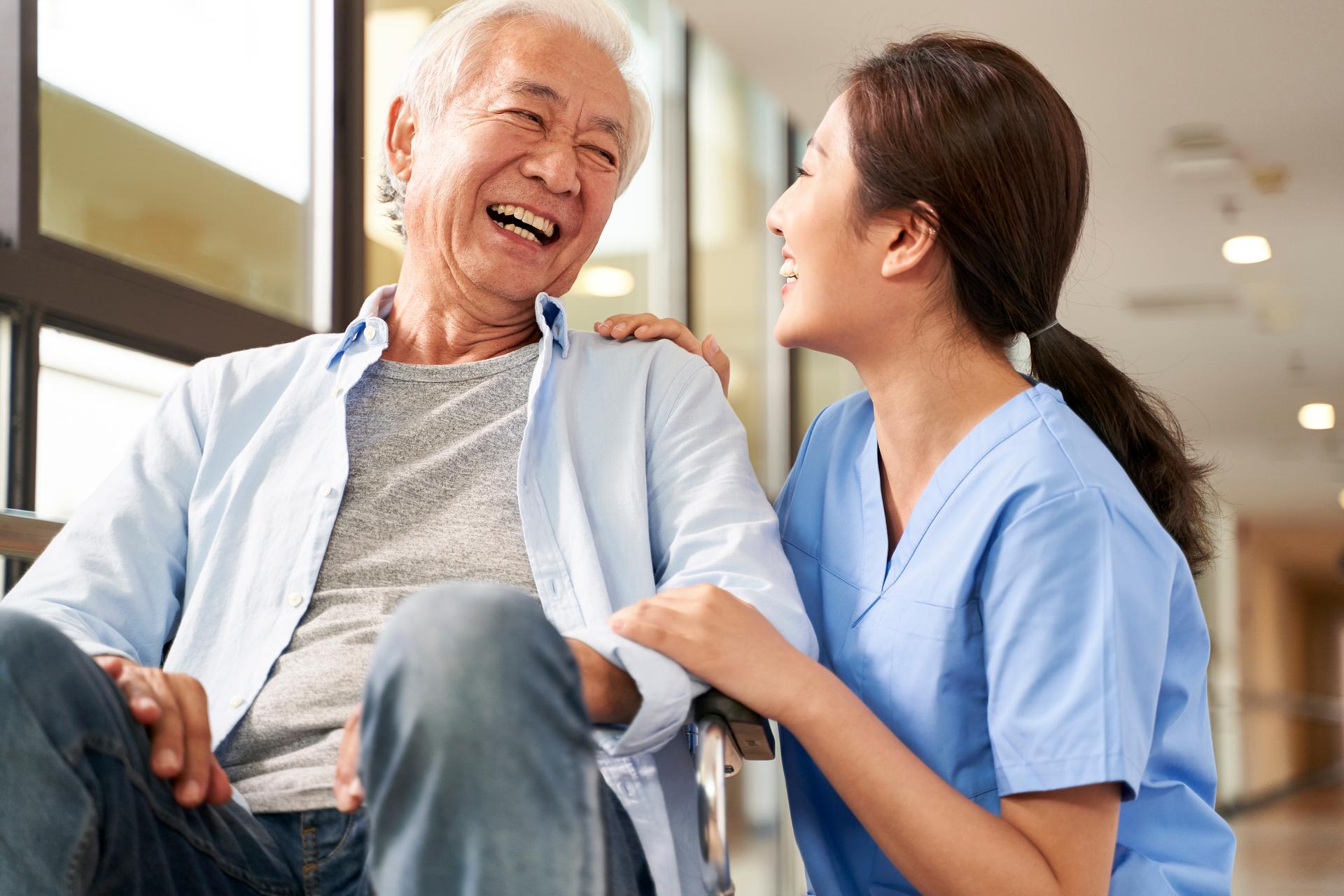 Nurse kneeling next to patient wheelchair; both are smiling and laughing