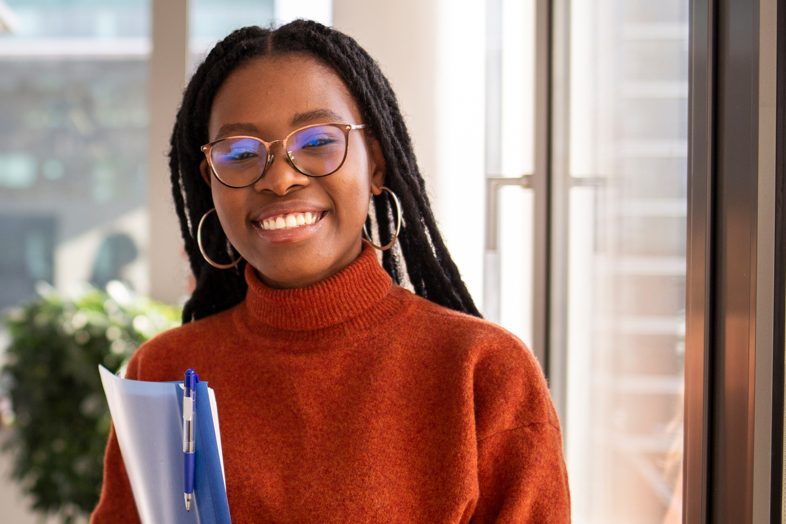 Young woman smiling to the camera, holding a file folder. 