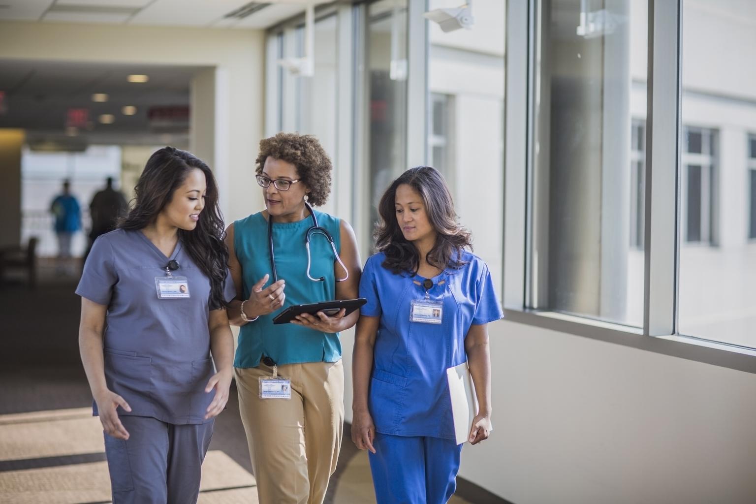 Nurse administrator and two new nurses walking through hospital cooridor, talking informally
