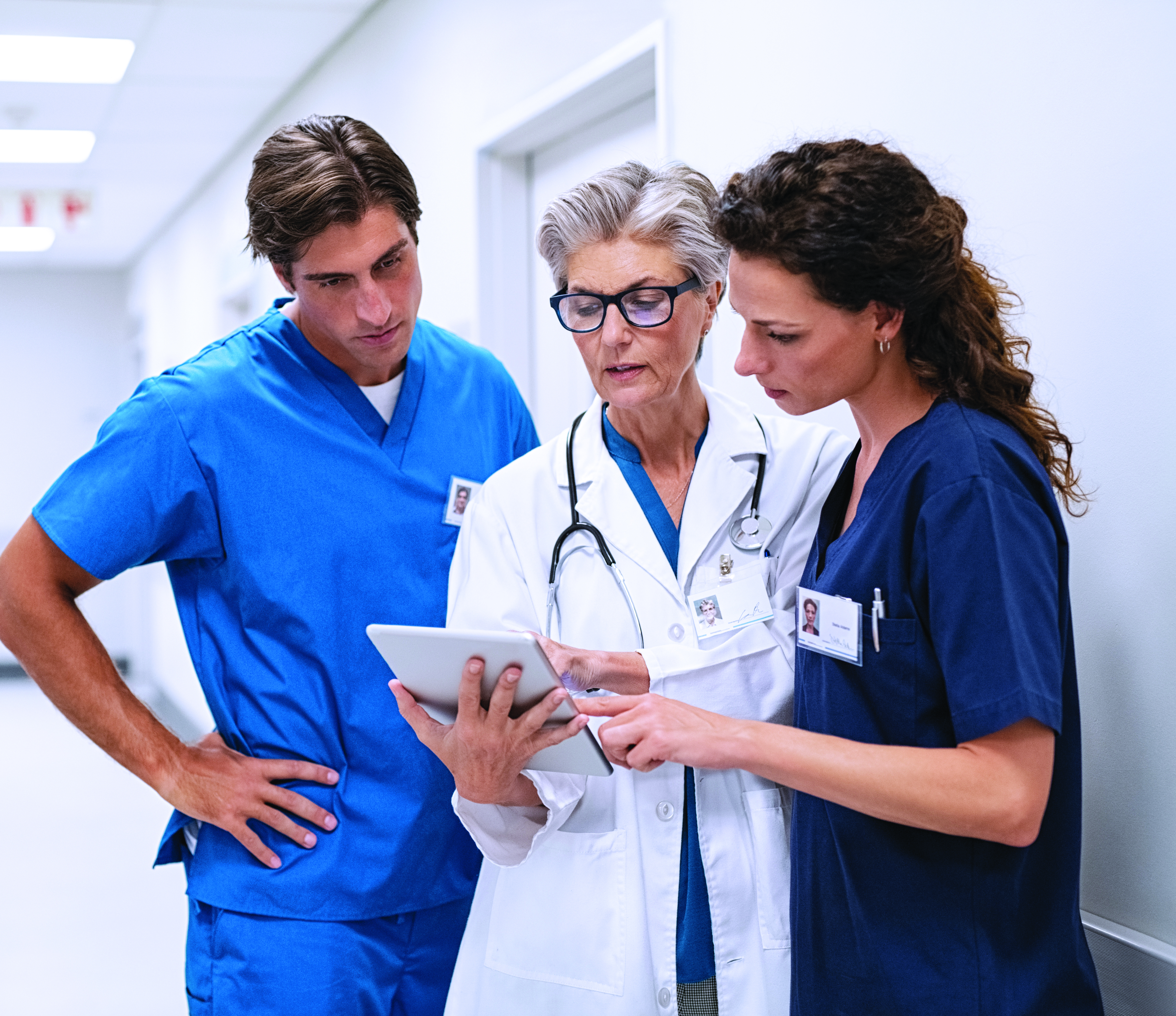 Three doctors huddled around tablet in the hallway of a medical facility