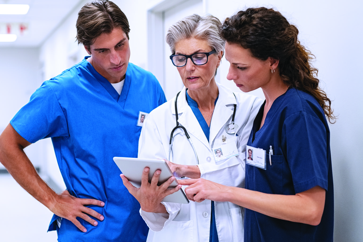 Three doctors huddled around tablet in the hallway of a medical facility