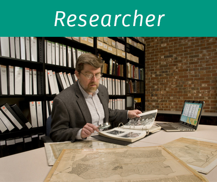 Researcher in archive, searching through maps and photographs