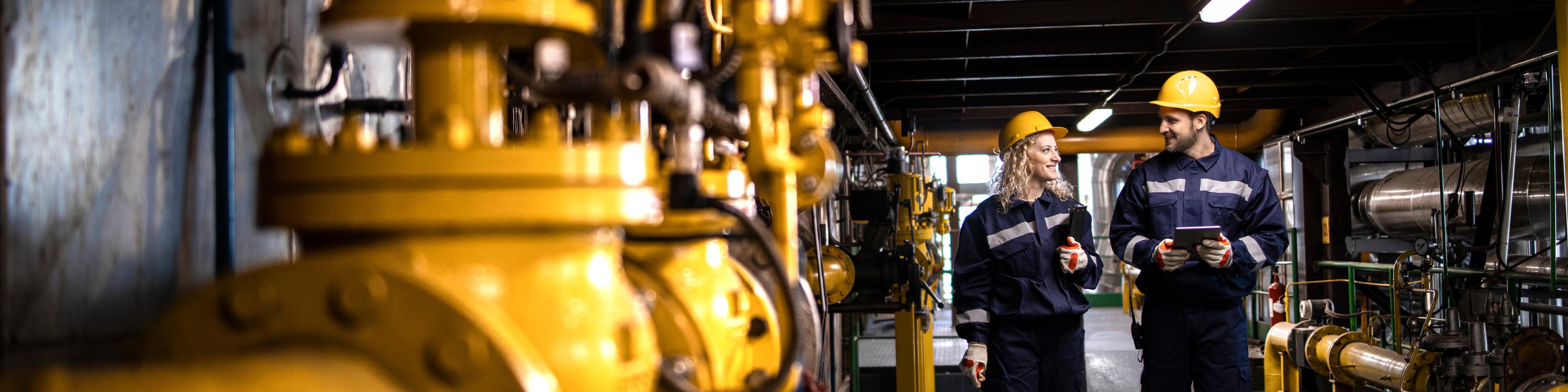 Oil and gas refinery production. Factory workers in safety equipment walking by gas pipes and checking distribution and consumption.