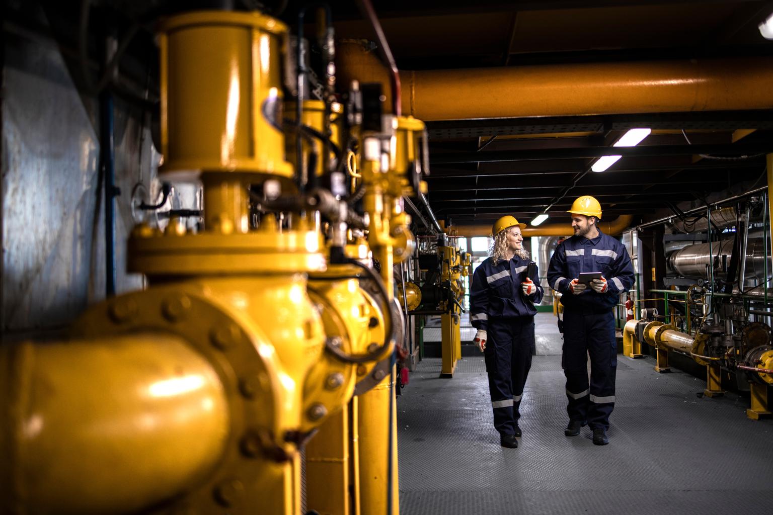 Oil and gas refinery production. Factory workers in safety equipment walking by gas pipes and checking distribution and consumption.