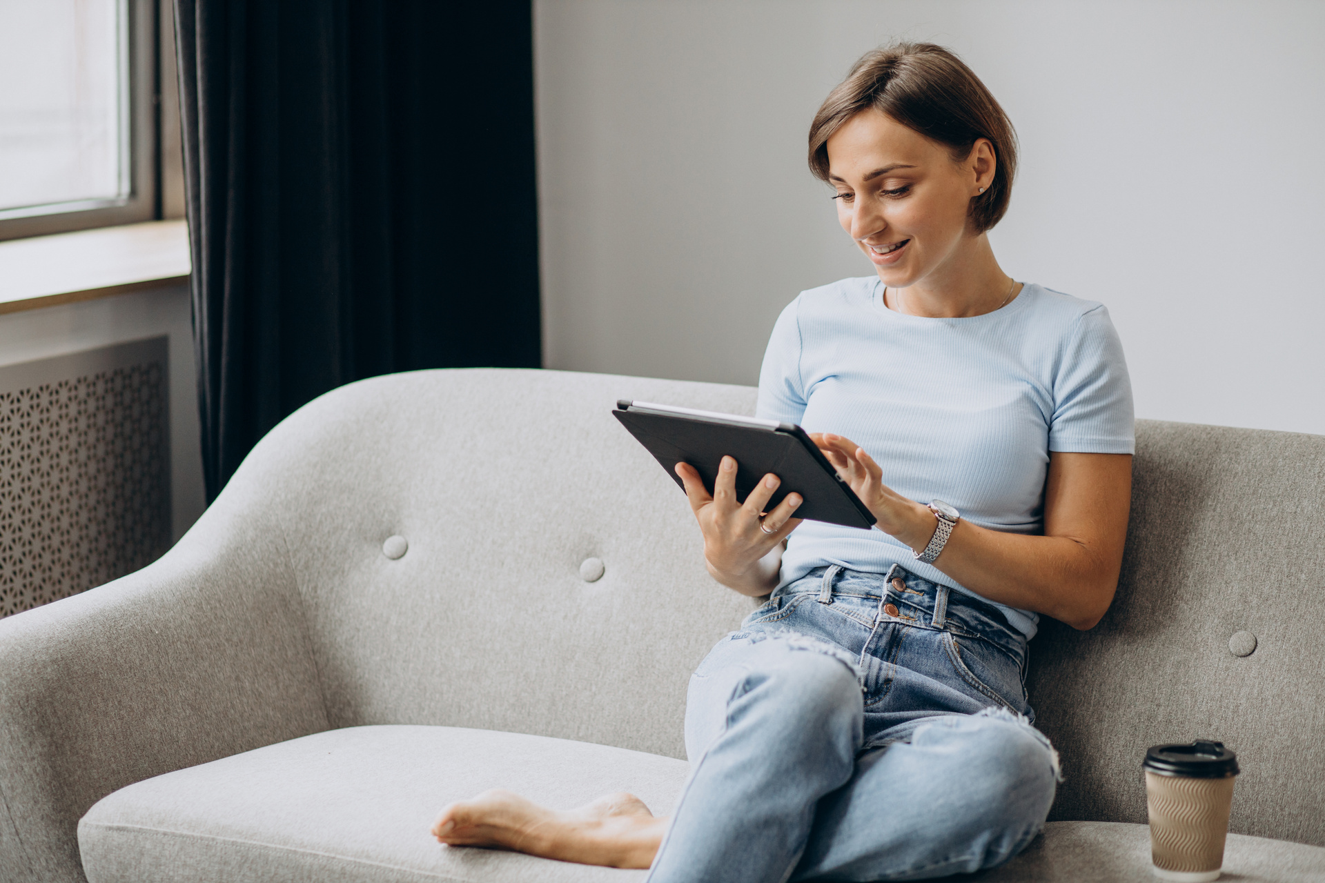 woman sitting home on a sofa and reading on a tablet