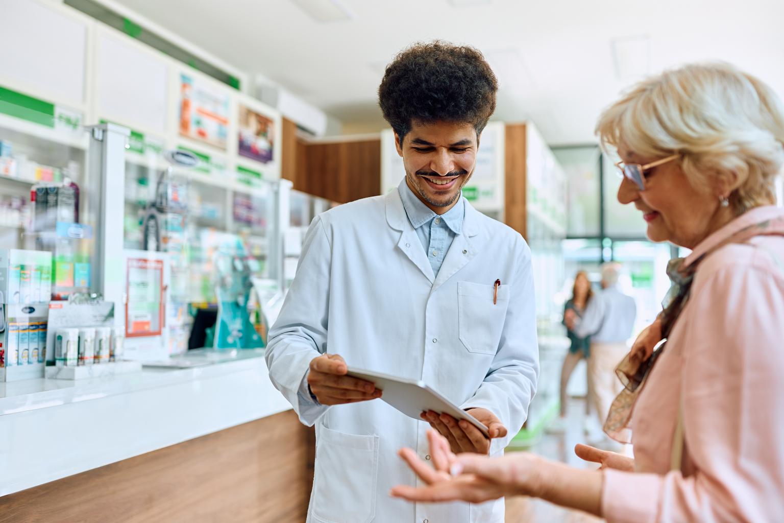 Pharmacist using touchpad while assisting senior woman in pharmacy