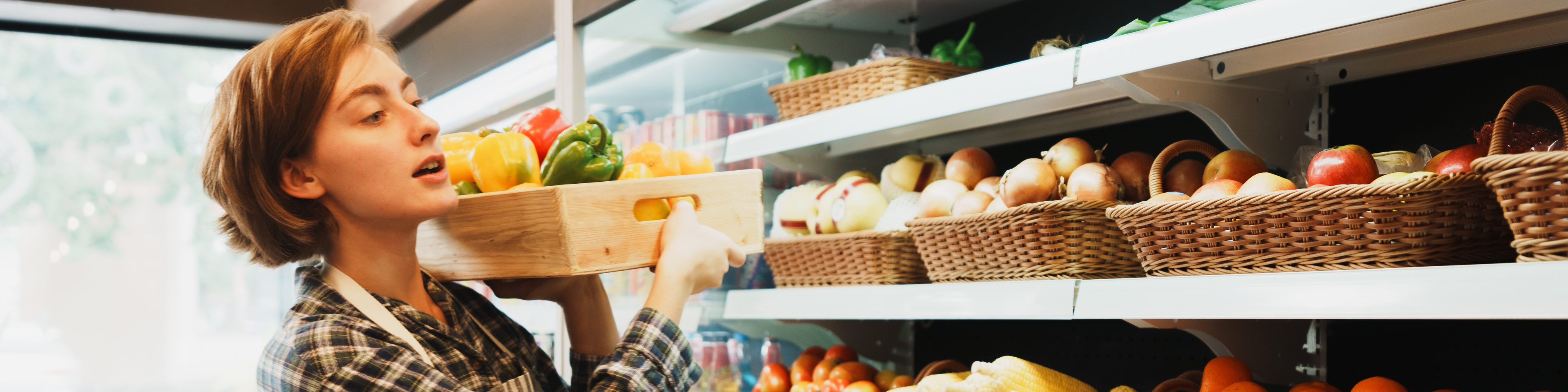 Female employee stacking fruit and vegetables on shelves in grocery store