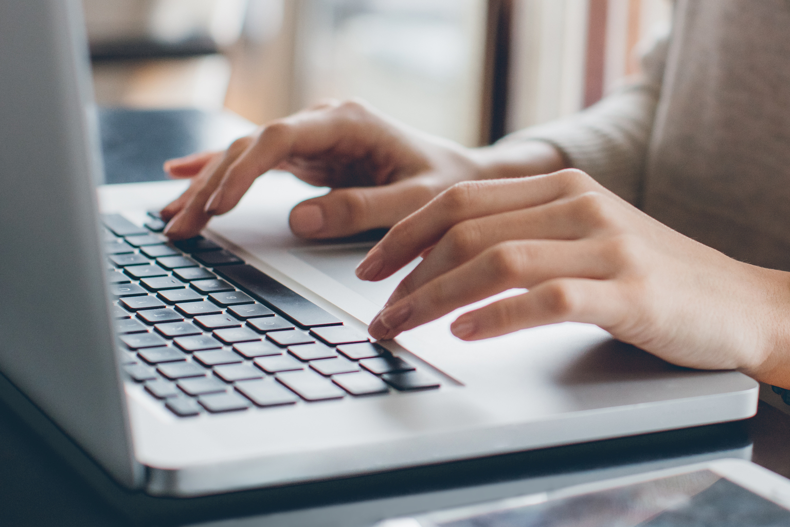 Woman with shoulder length hair and grey sweater sitting down using laptop, black and white face watch on left hand, Q3 2021, TAA NA US - Preparer