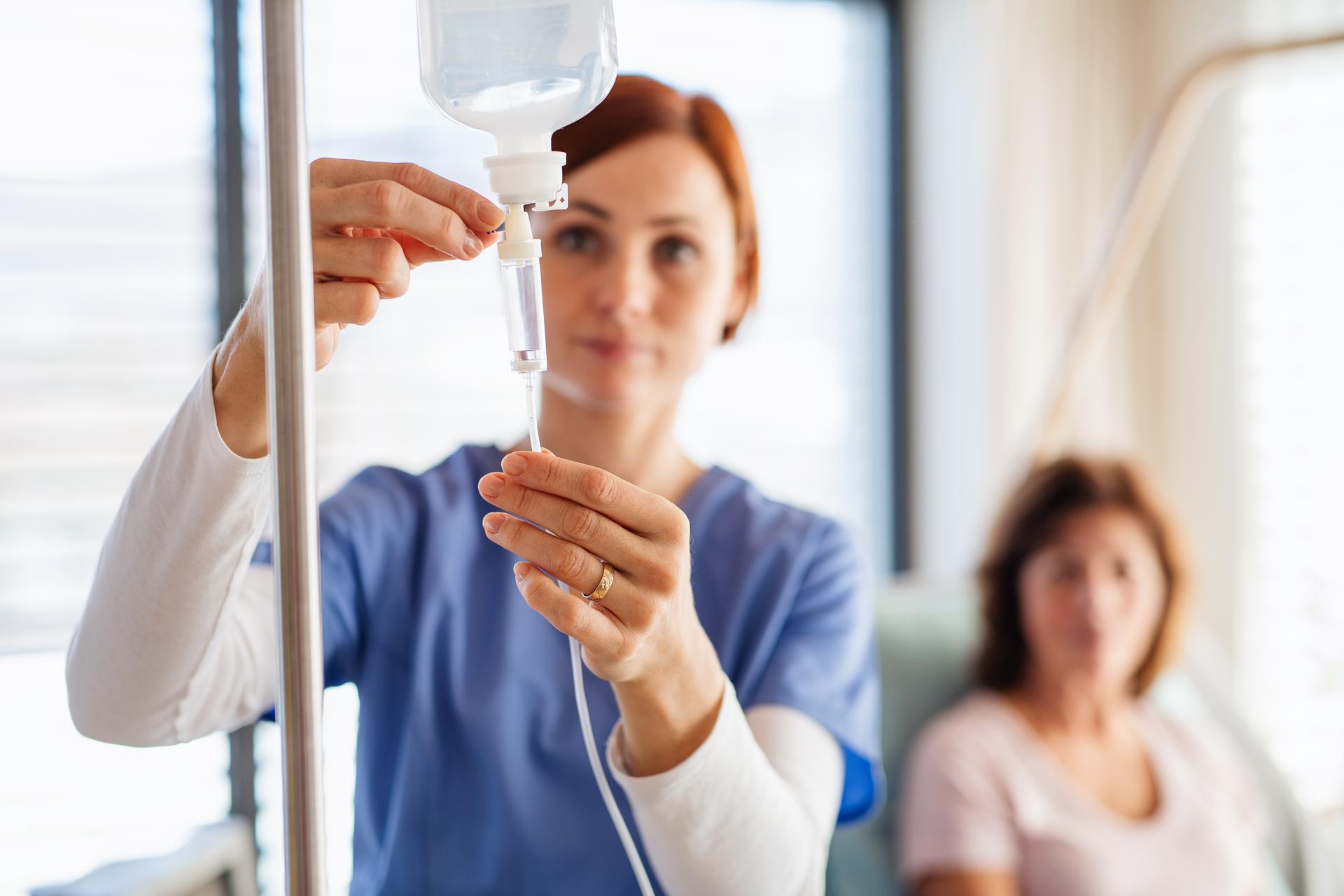 Nurse adjusting intravenous fluid line, patient blurred in background