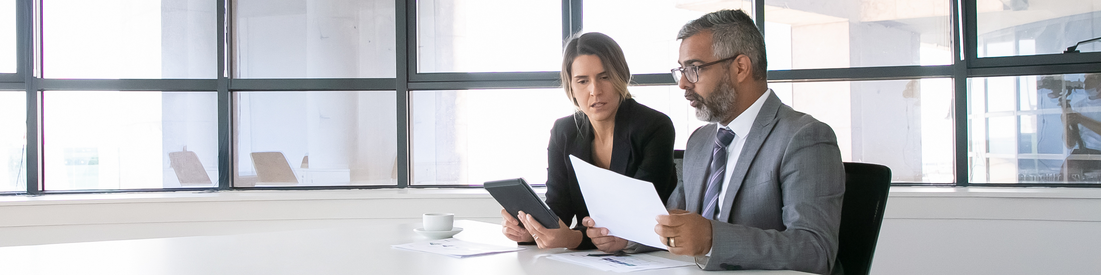 Two-business-colleagues-sitting-together-looking-at-document-holding-tablet-and-talking