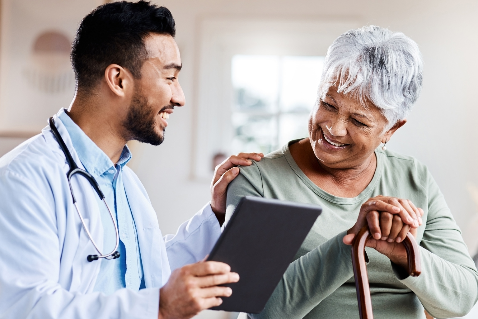 A doctor sharing information from his digital tablet with an older patient, reassuring that there is nothing to worry about.