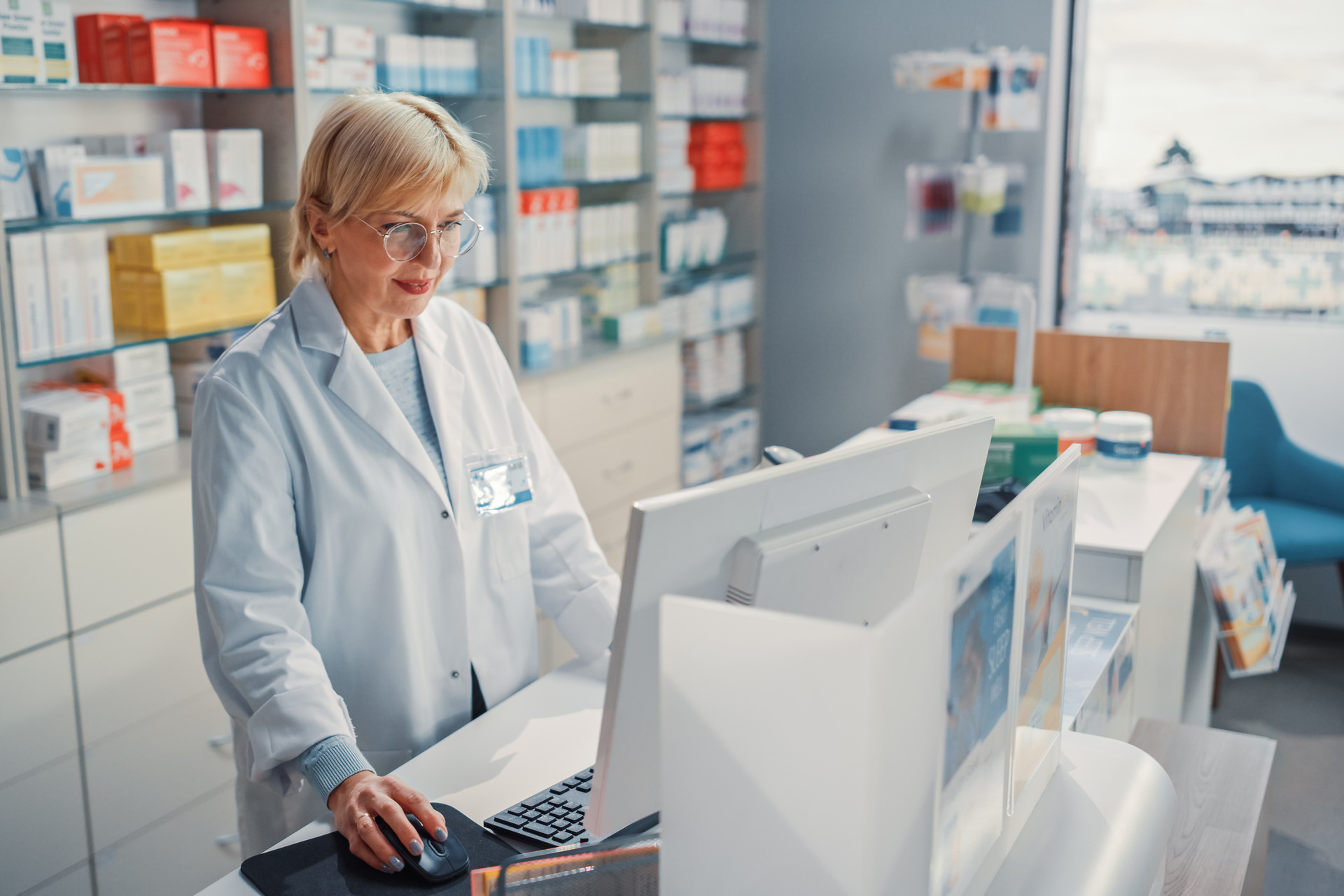 Pharmacist at a drugstore checkout counter, using a computer to check stock inventory of medicine, drugs, vitamins, and health care products.