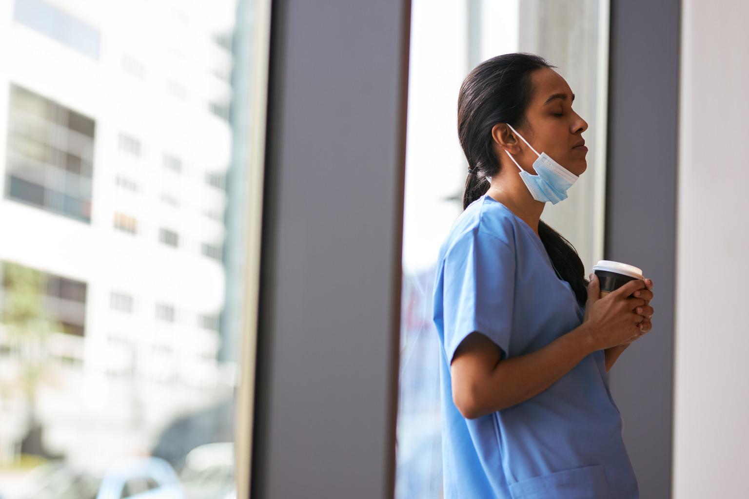 Overworked nurse in scrubs with face mask takes coffee break in busy hospital during health pandemic