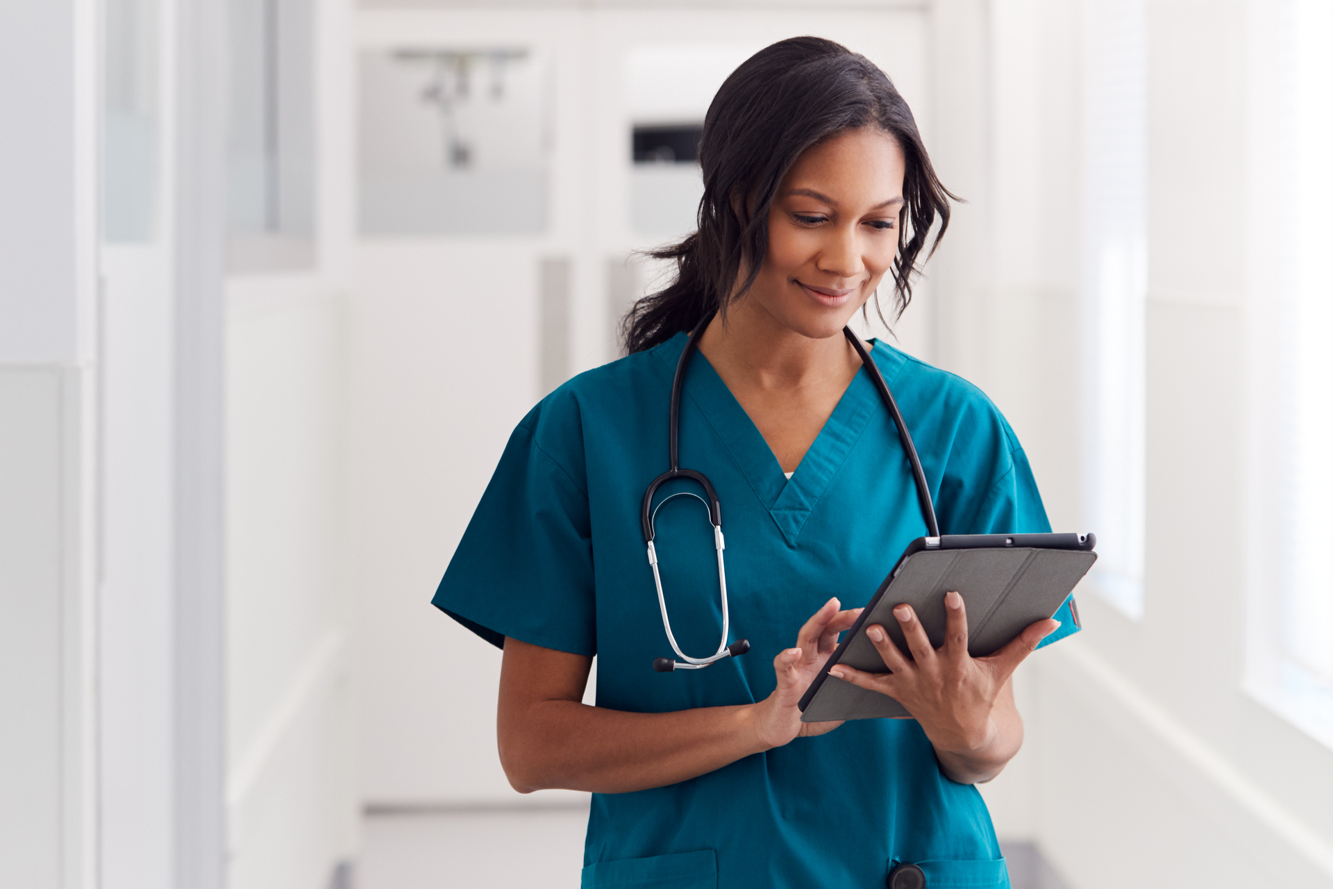 Nurse in hospital hallway reading on a tablet device