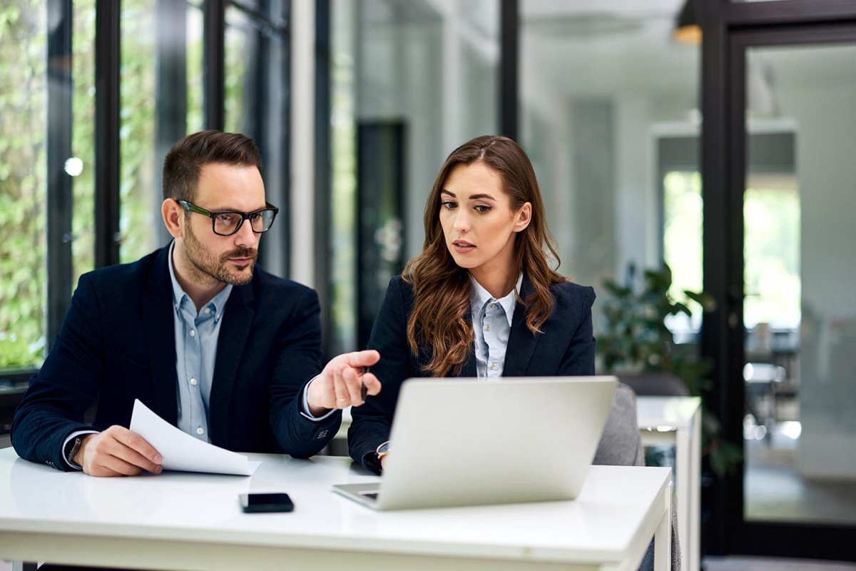 Hardworking female and male employees sitting at the office table and working together over a laptop.