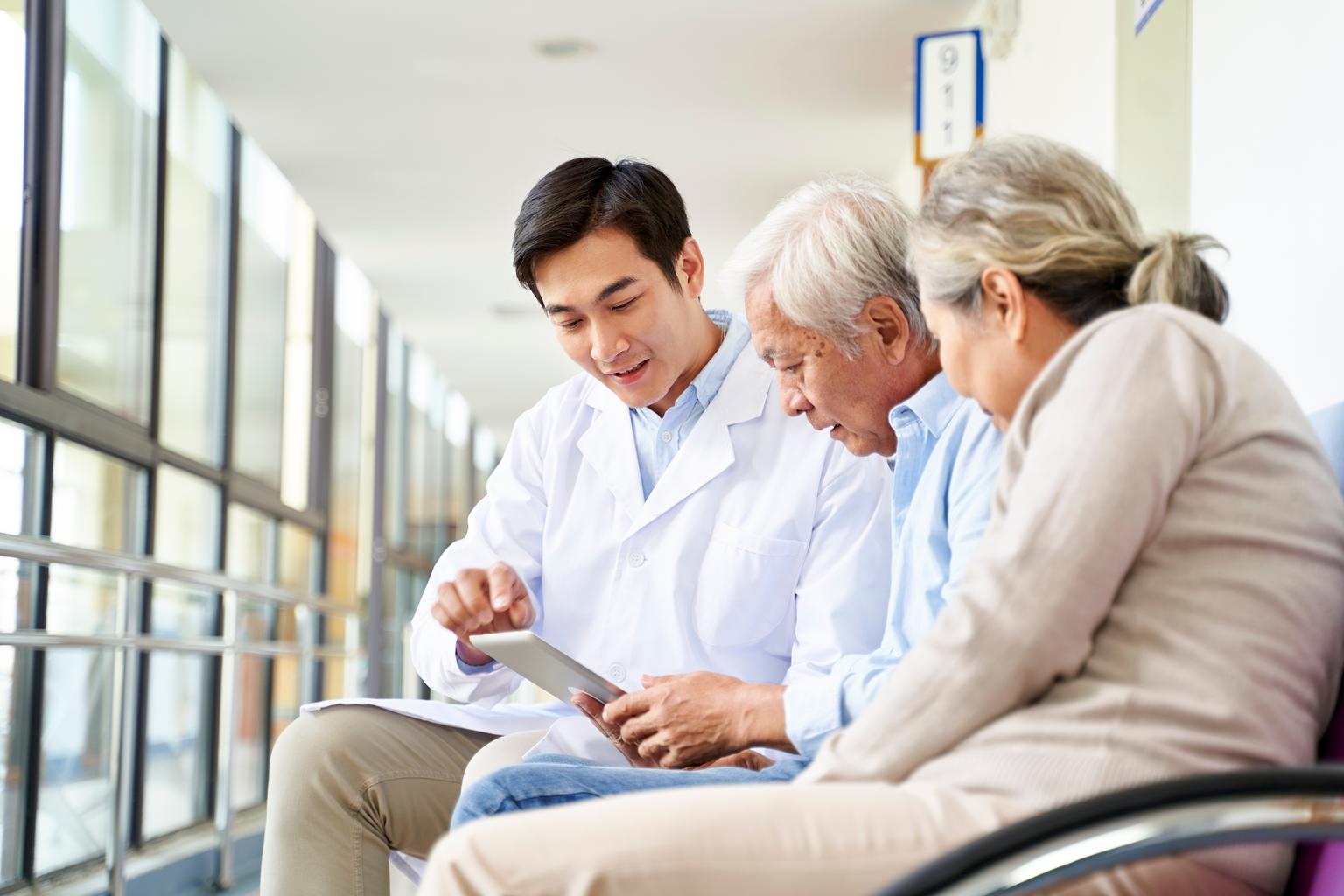 Young asian doctor talking to senior couple patients in hospital hallway