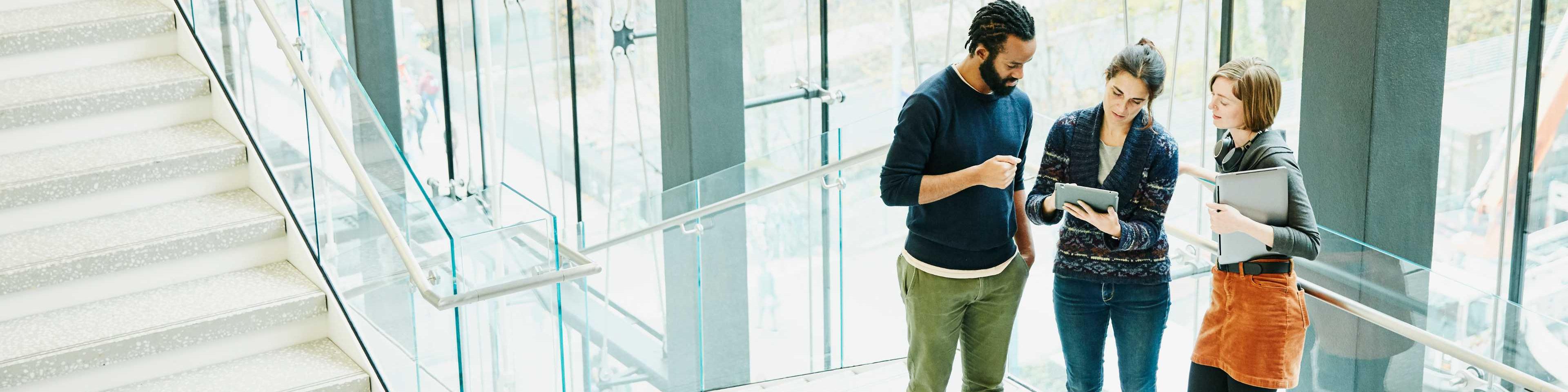 Man and two women reviewing tablet in office stairway