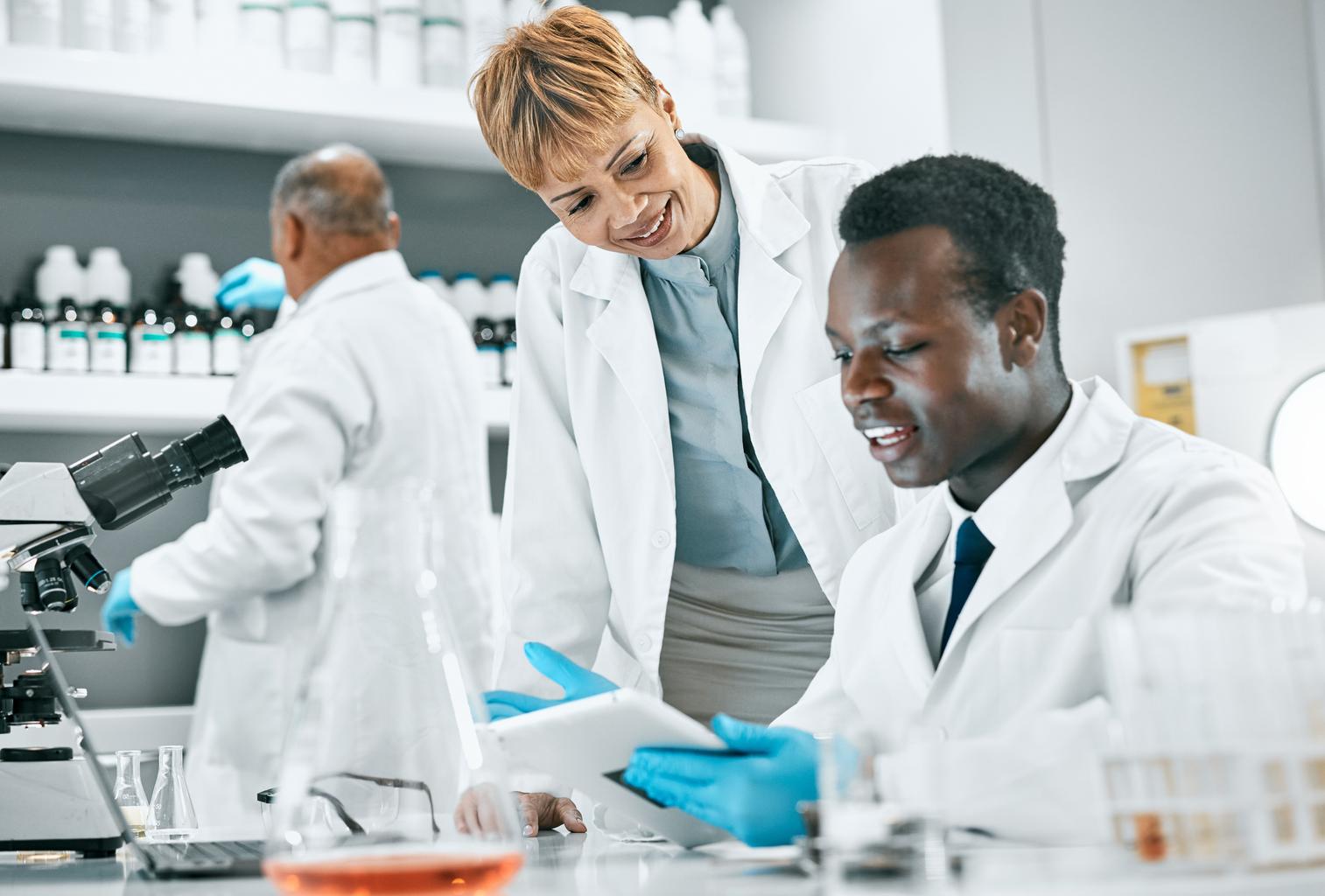 Medical professionals working together in a laboratory setting, analyzing DNA research data on a tablet