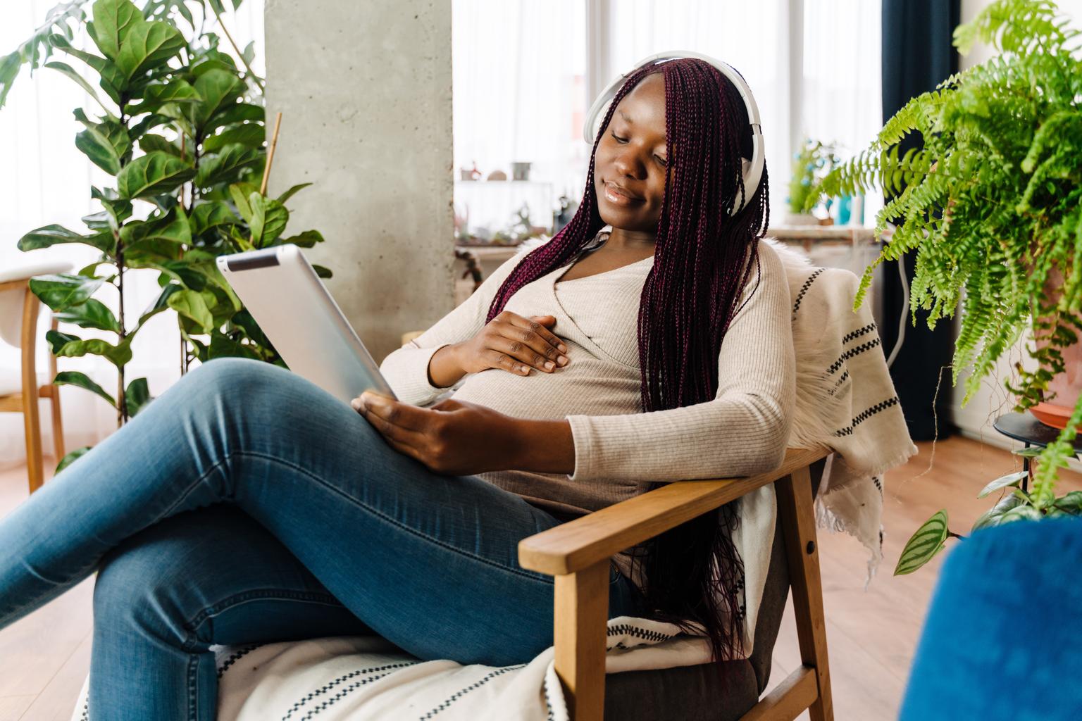 Pregnant black woman listening to music using a tablet