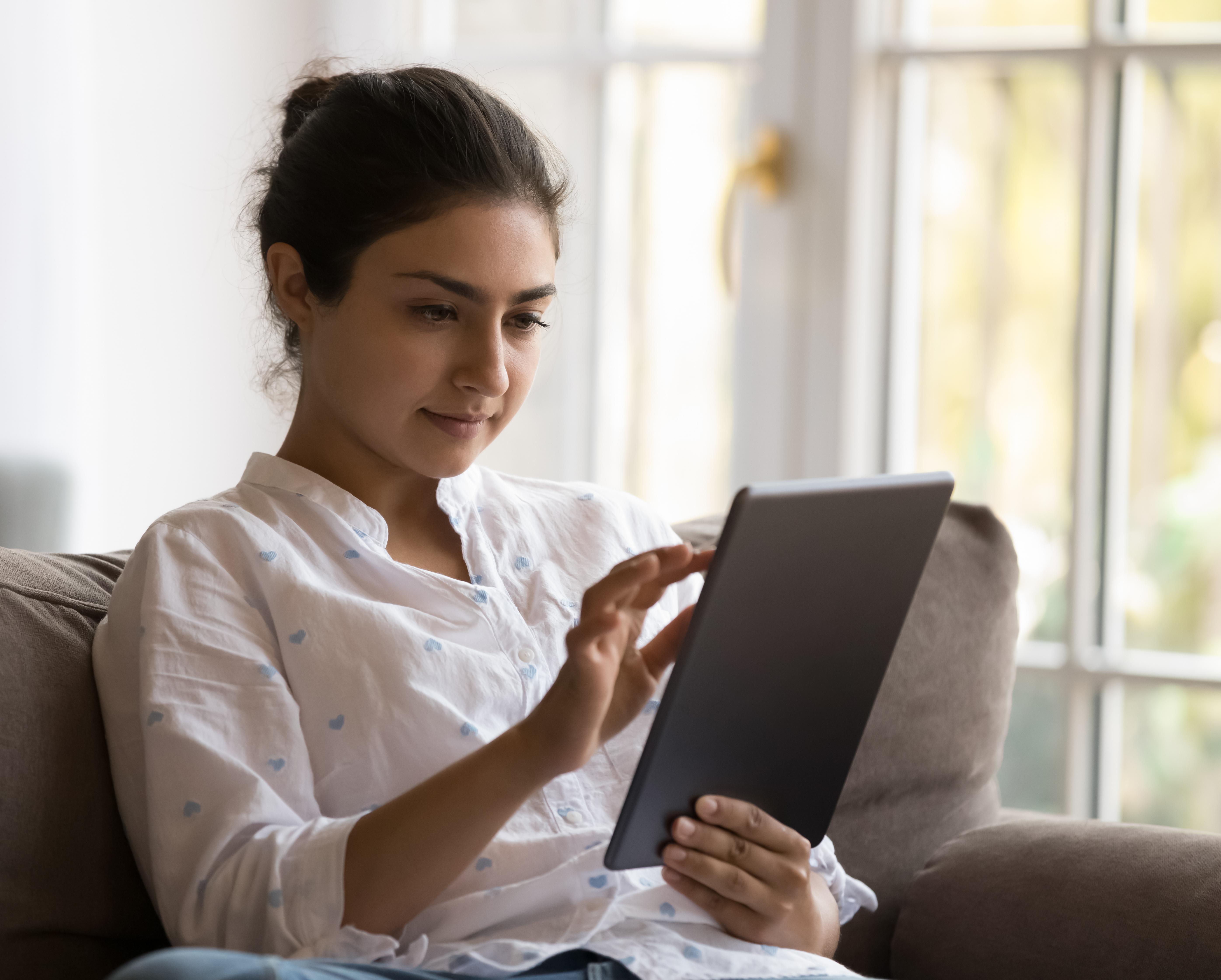 Portrait of an Indian woman sitting on a sofa at home using a tablet