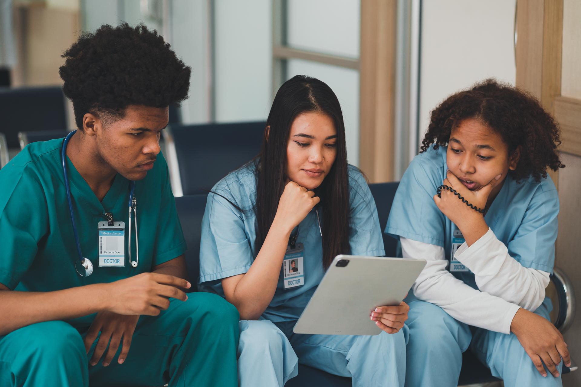 Nursing students sit three in a row, reviewing class assignment on tablet