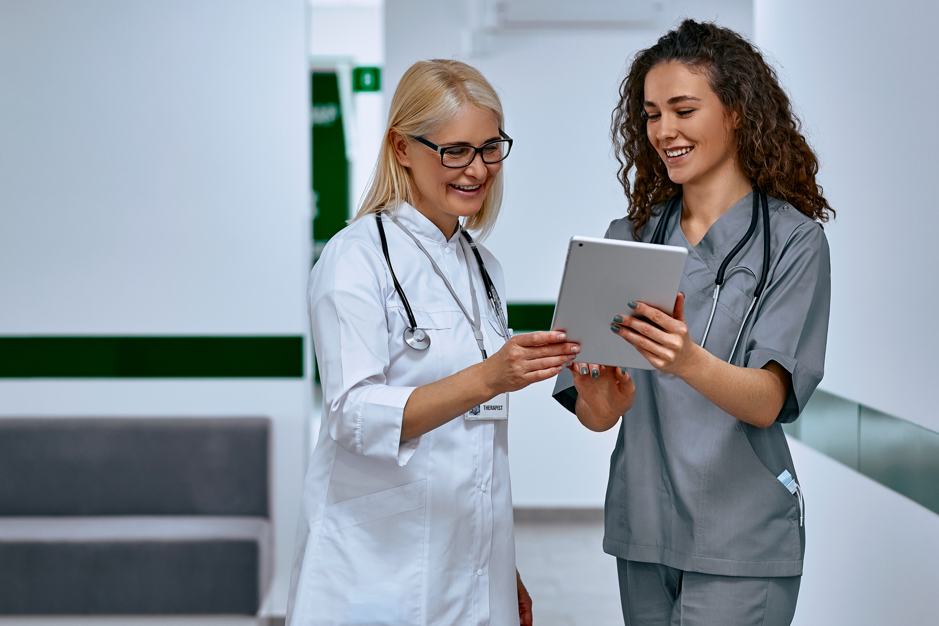 A nurse wearing grey scrubs show's patient information to medical colleague