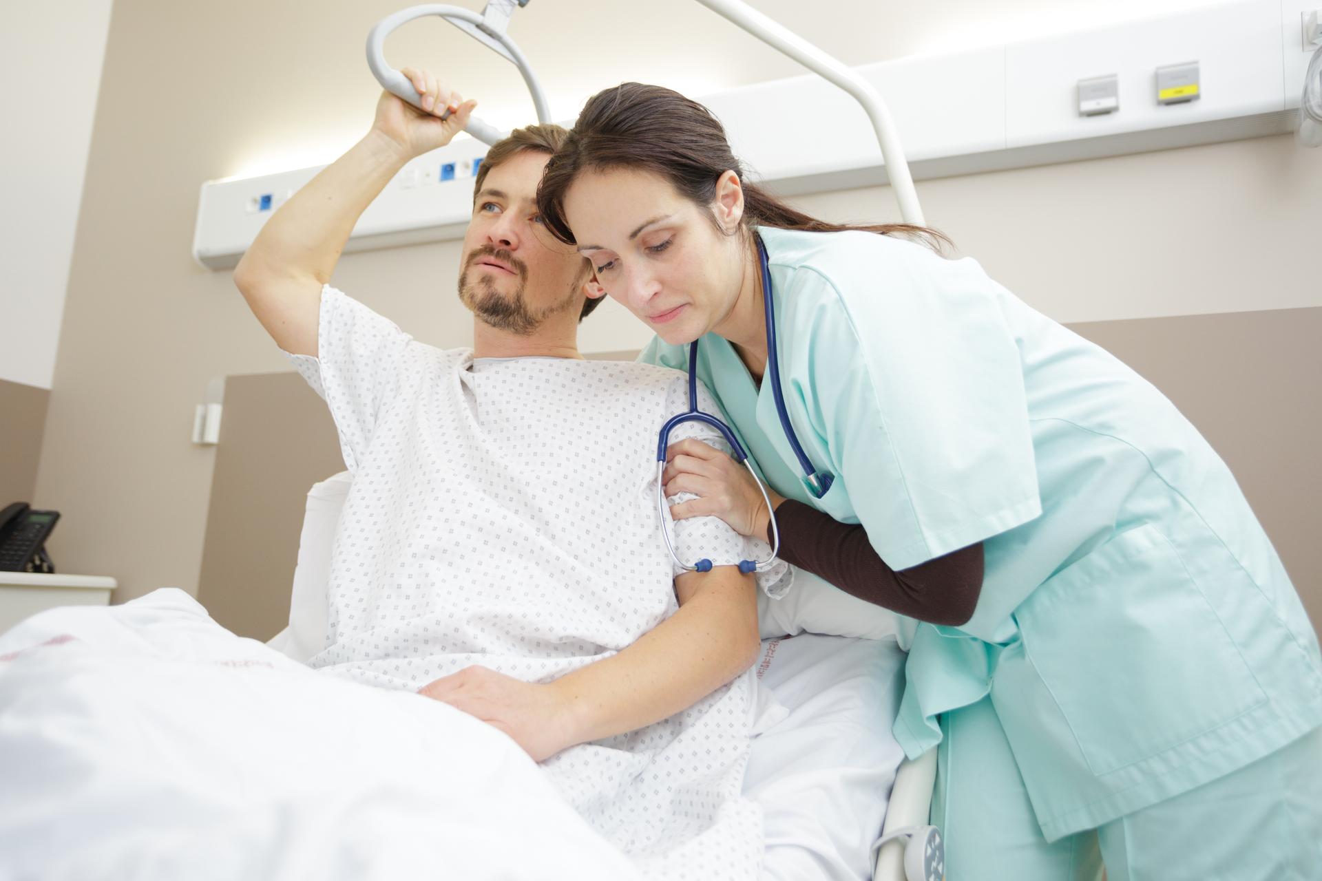 Nurse assisting partially paralyzed patient getting into the hospital bed.