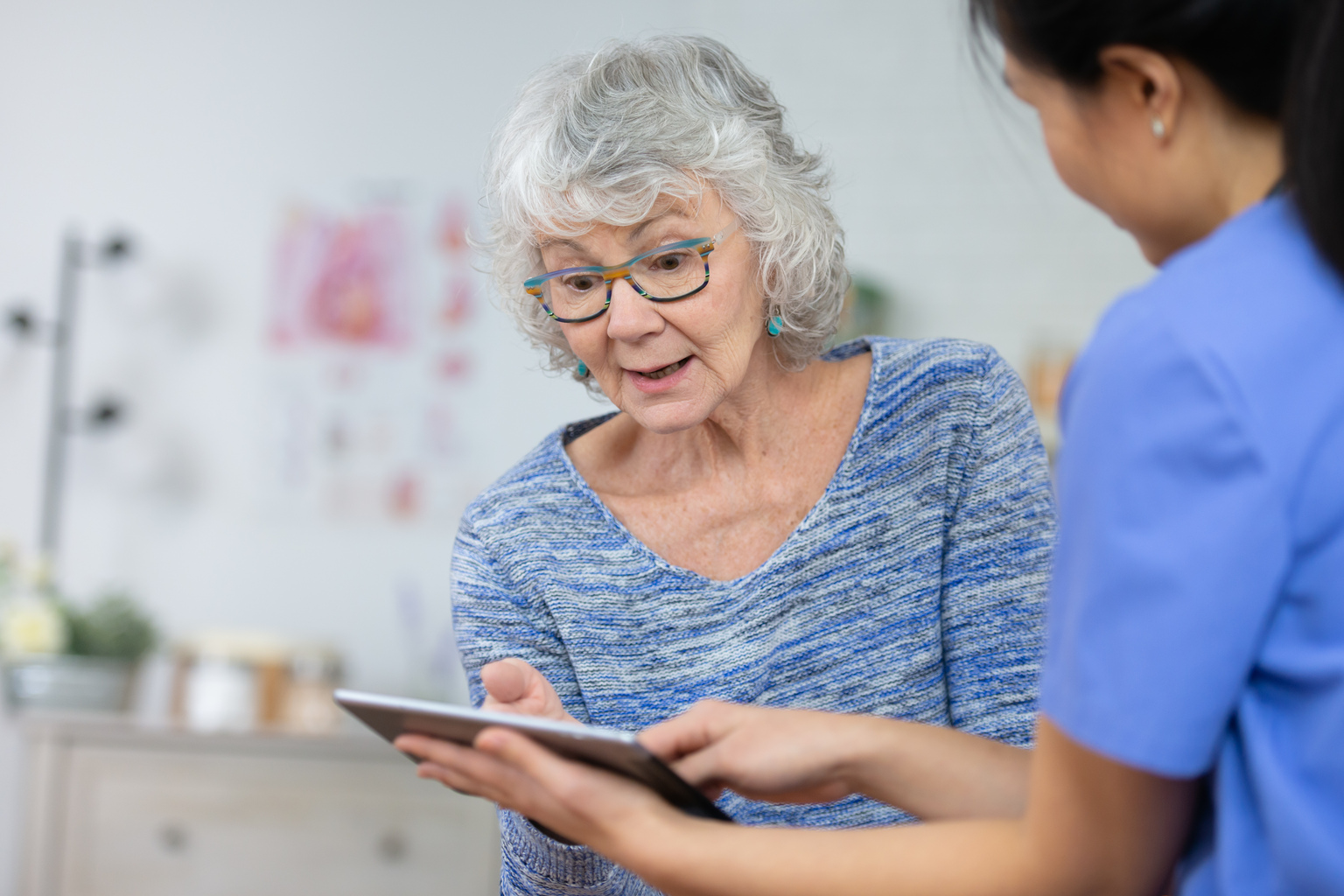 Female nurse shows senior female patient results on tablet.