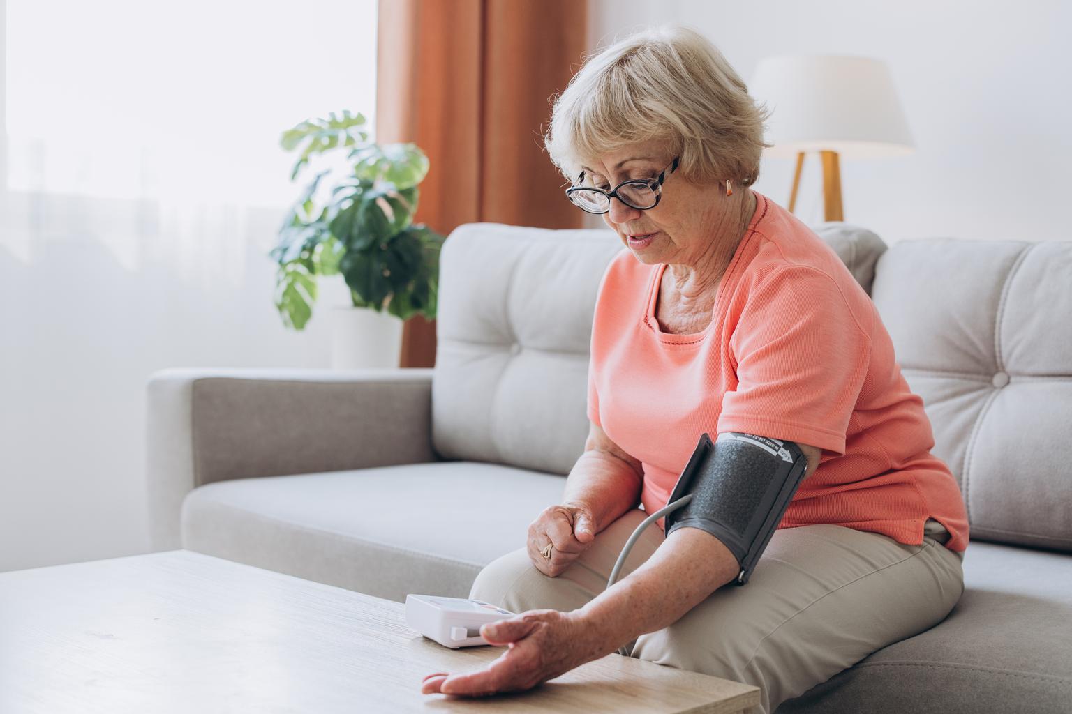 Senior elderly woman measuring blood pressure using tonometer at home