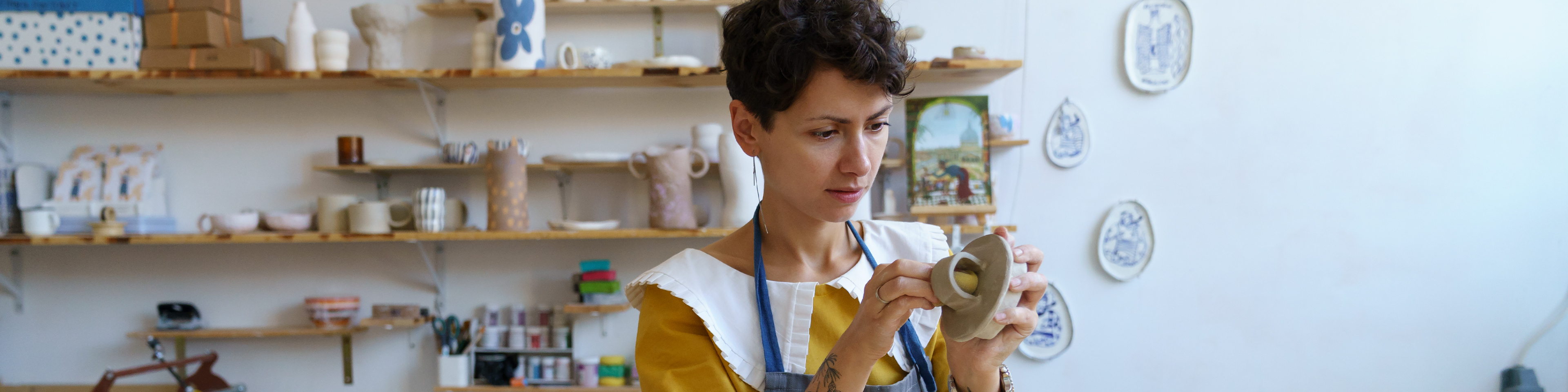 Woman potter holding paintbrush, painting on clay jug.jpeg