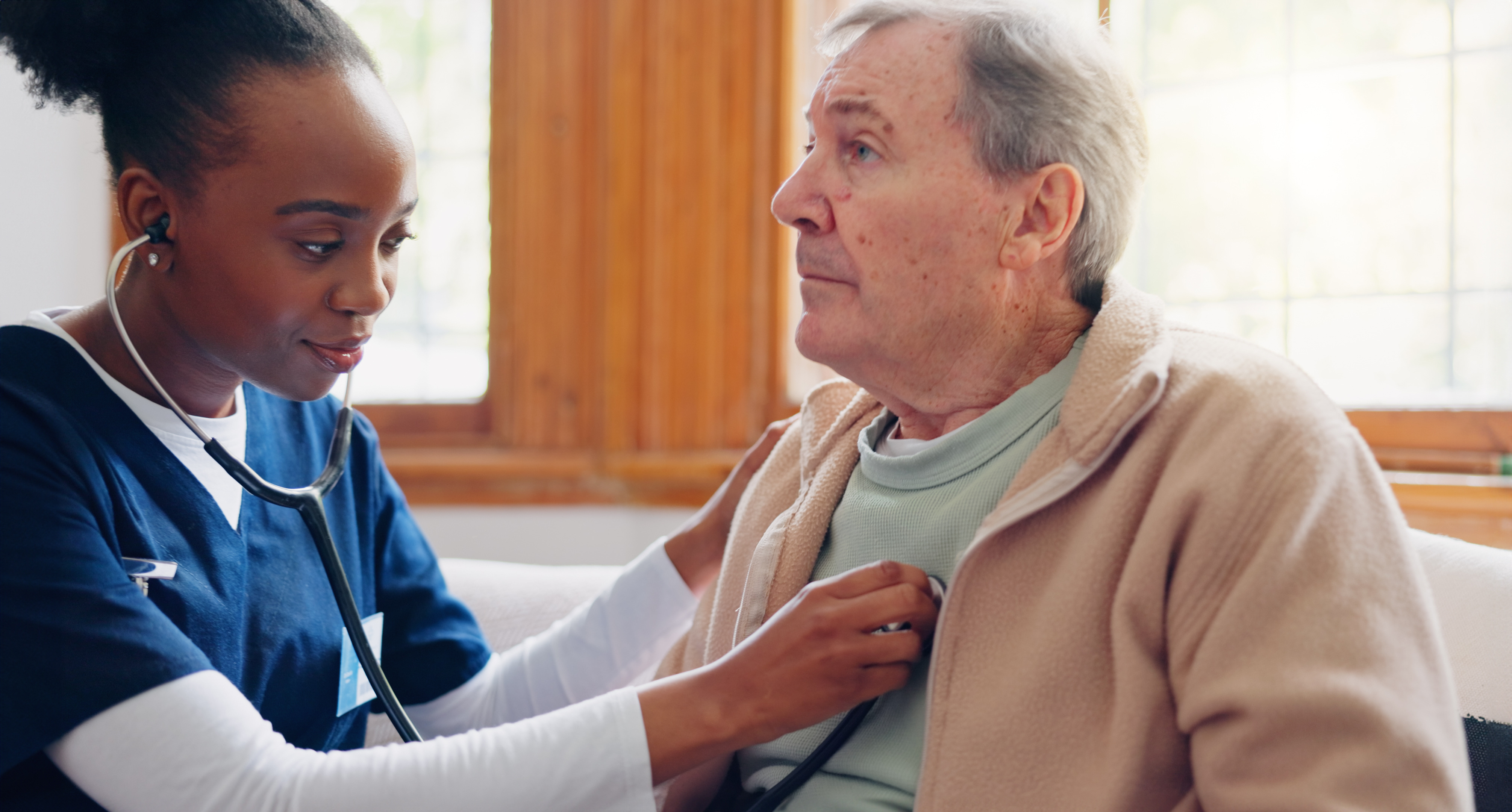 Woman caregiver checking the heart of senior male patient in a retirement home