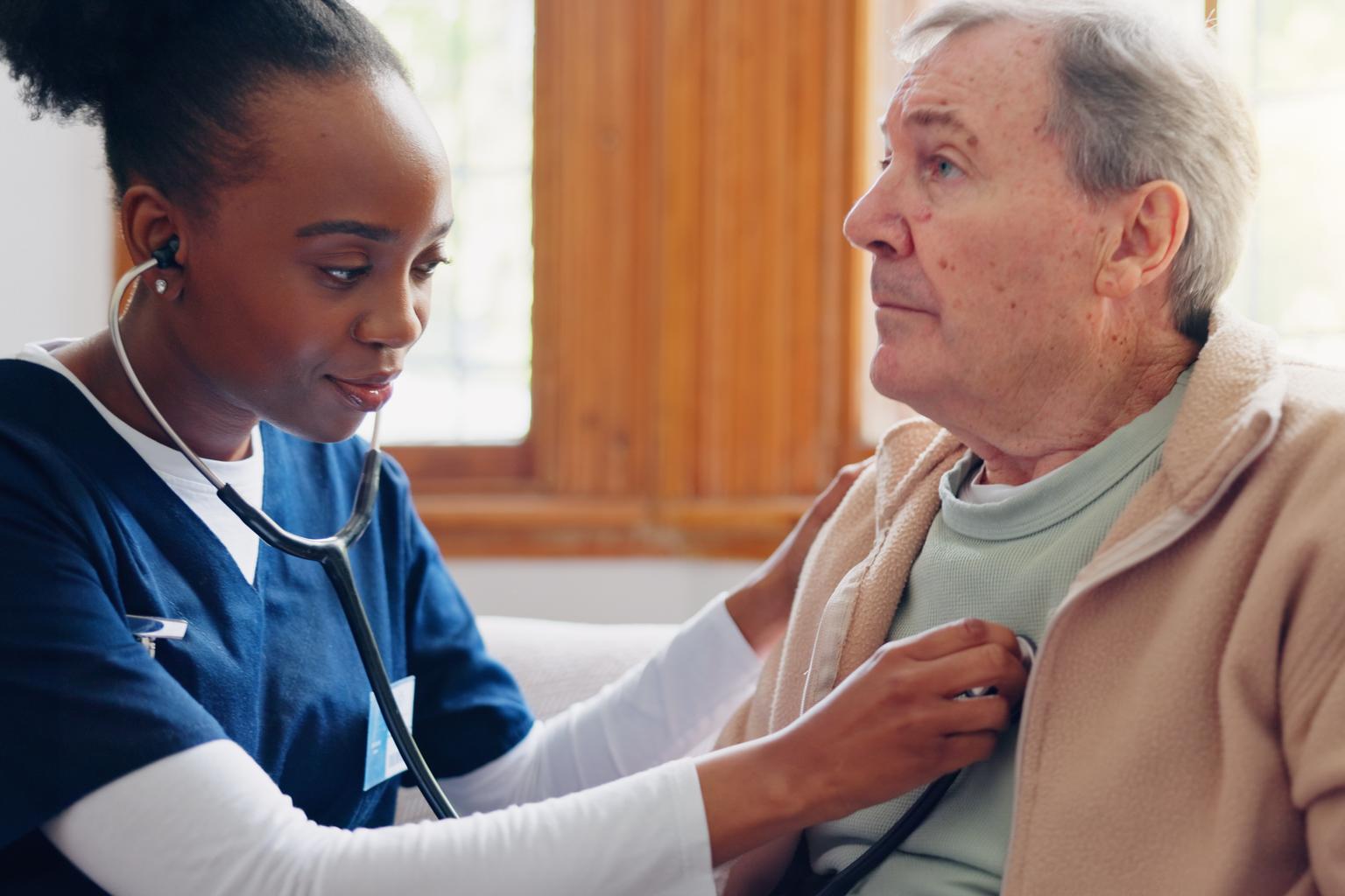 Woman caregiver checking the heart of senior male patient in a retirement home