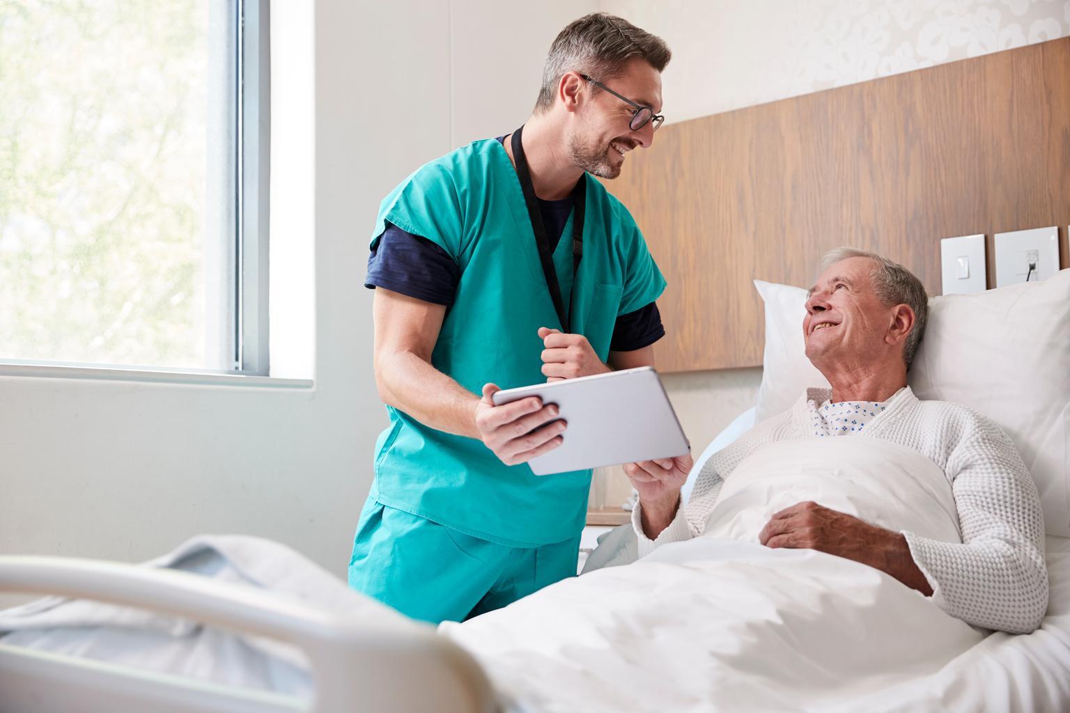 Male surgeon with tablet visiting senior male patient in hospital bed