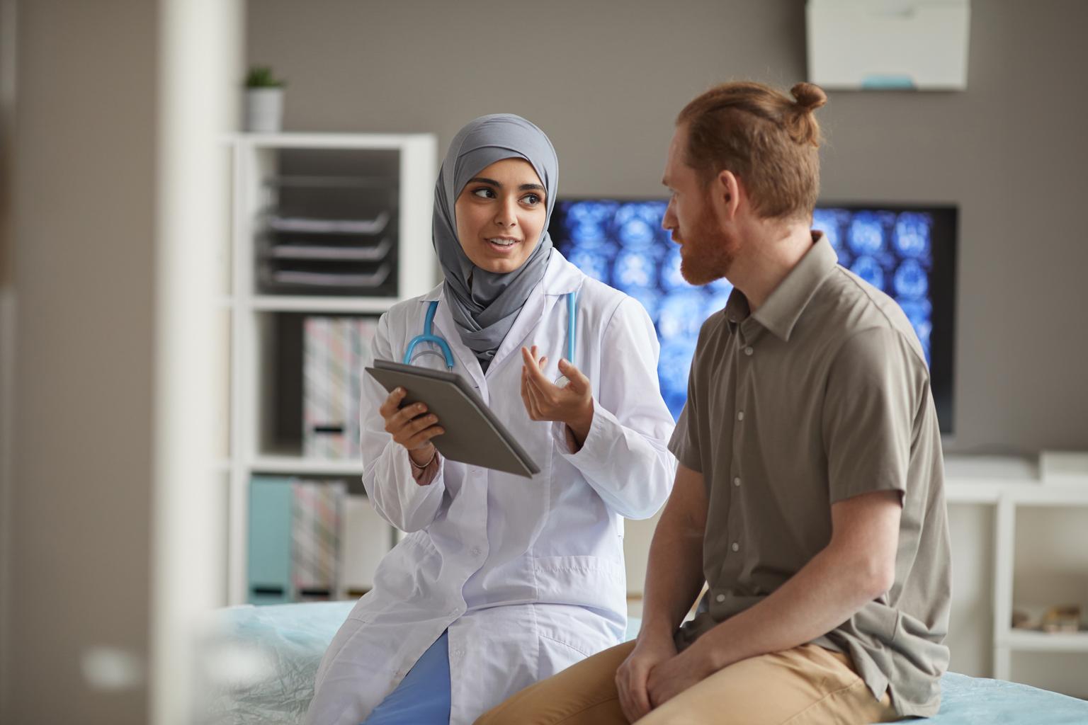 A male patient listens attentively to his doctor as she explains using a digital tablet in a hospital.