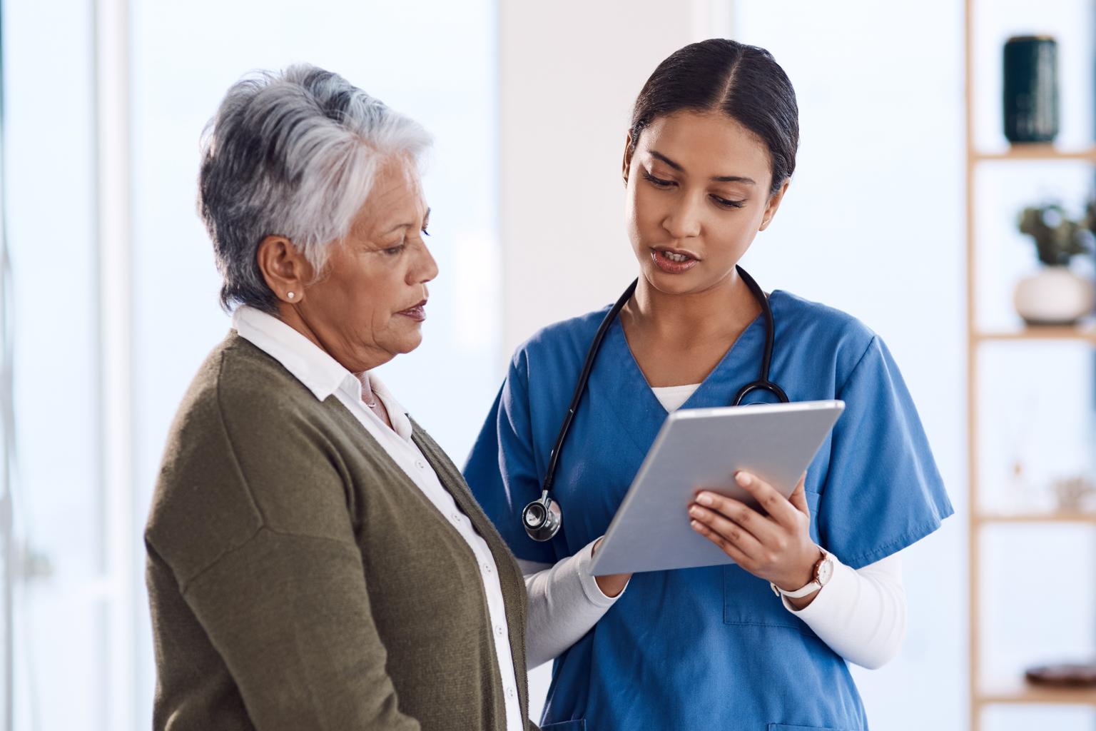 Young female doctor using a tablet during consultation with a senior woman