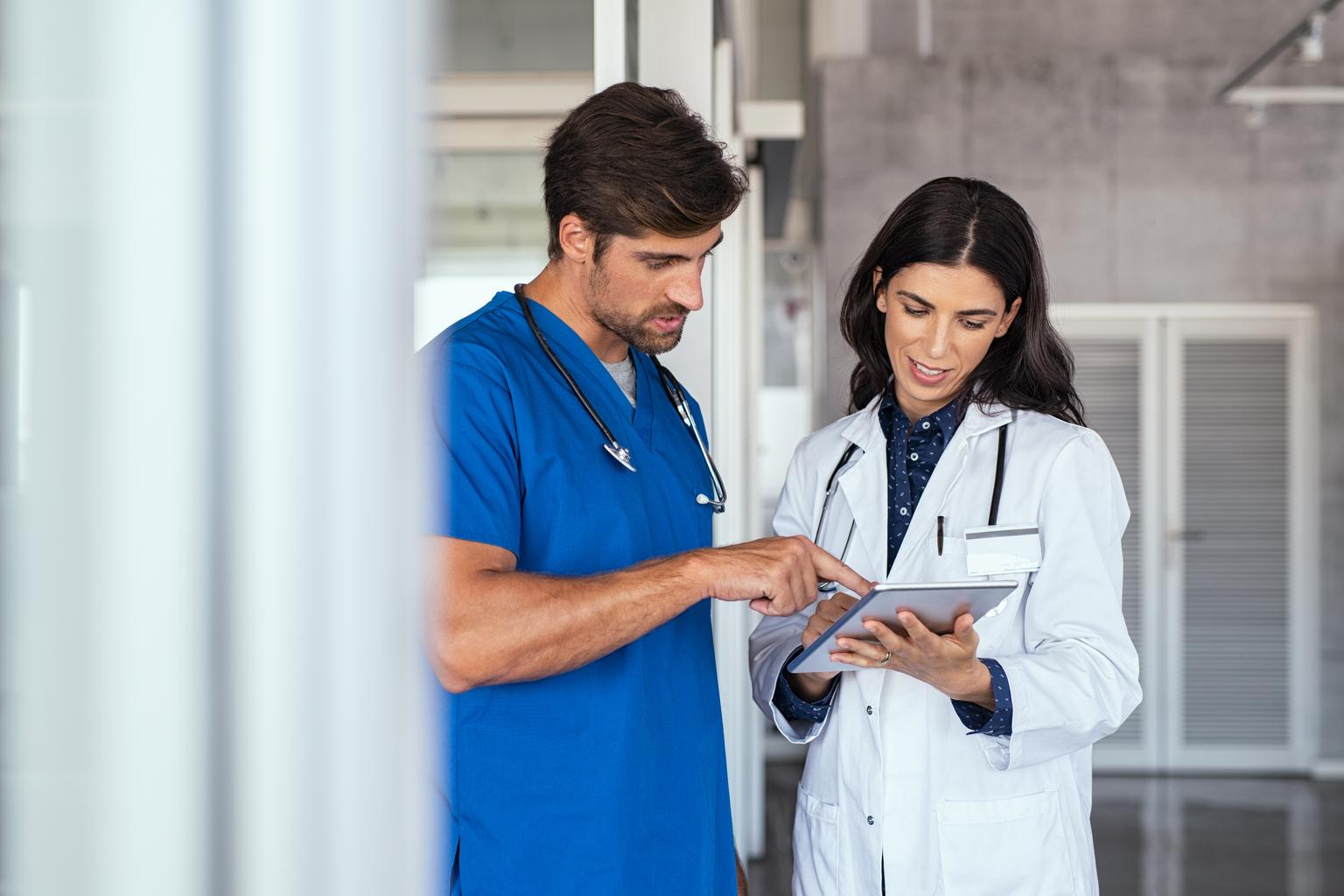 Two medical professionals huddled together informally in the hallway discuss patient care, using a tablet