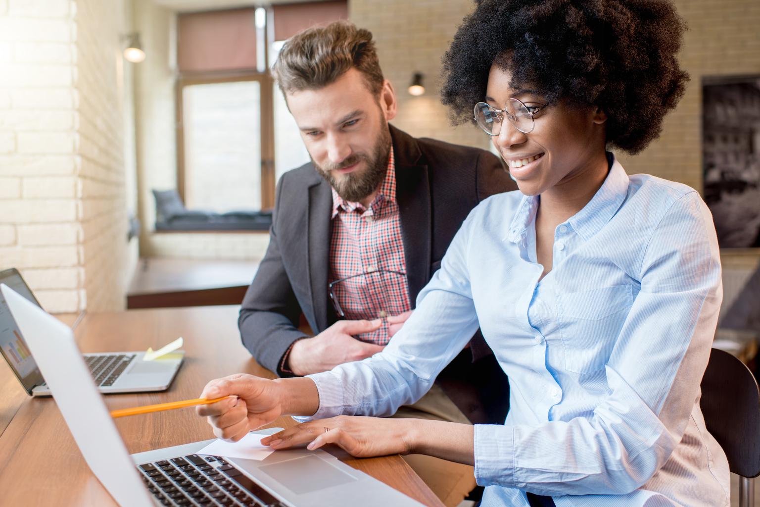 Businesswoman and man working together with laptops near the window at the office 