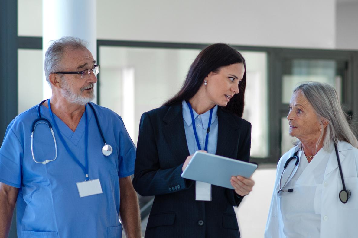 A hospital administrator and two healthcare professionals review patient information on tablet in hospital wing