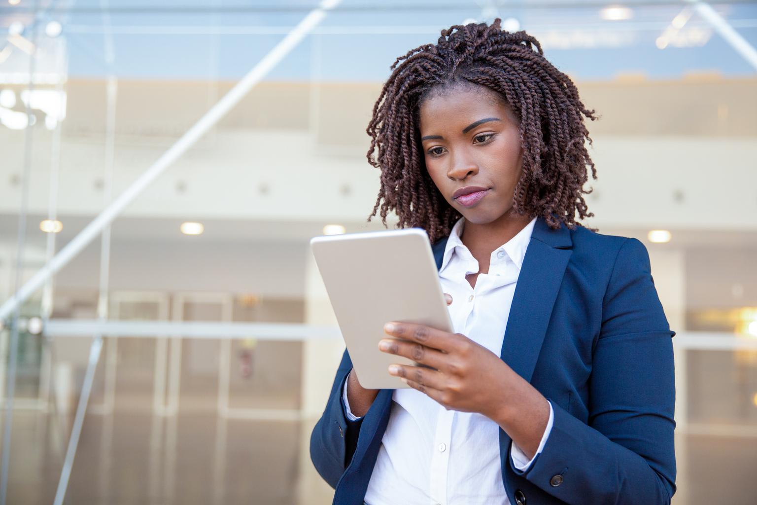 A focused business women using app on digital tablet outside.