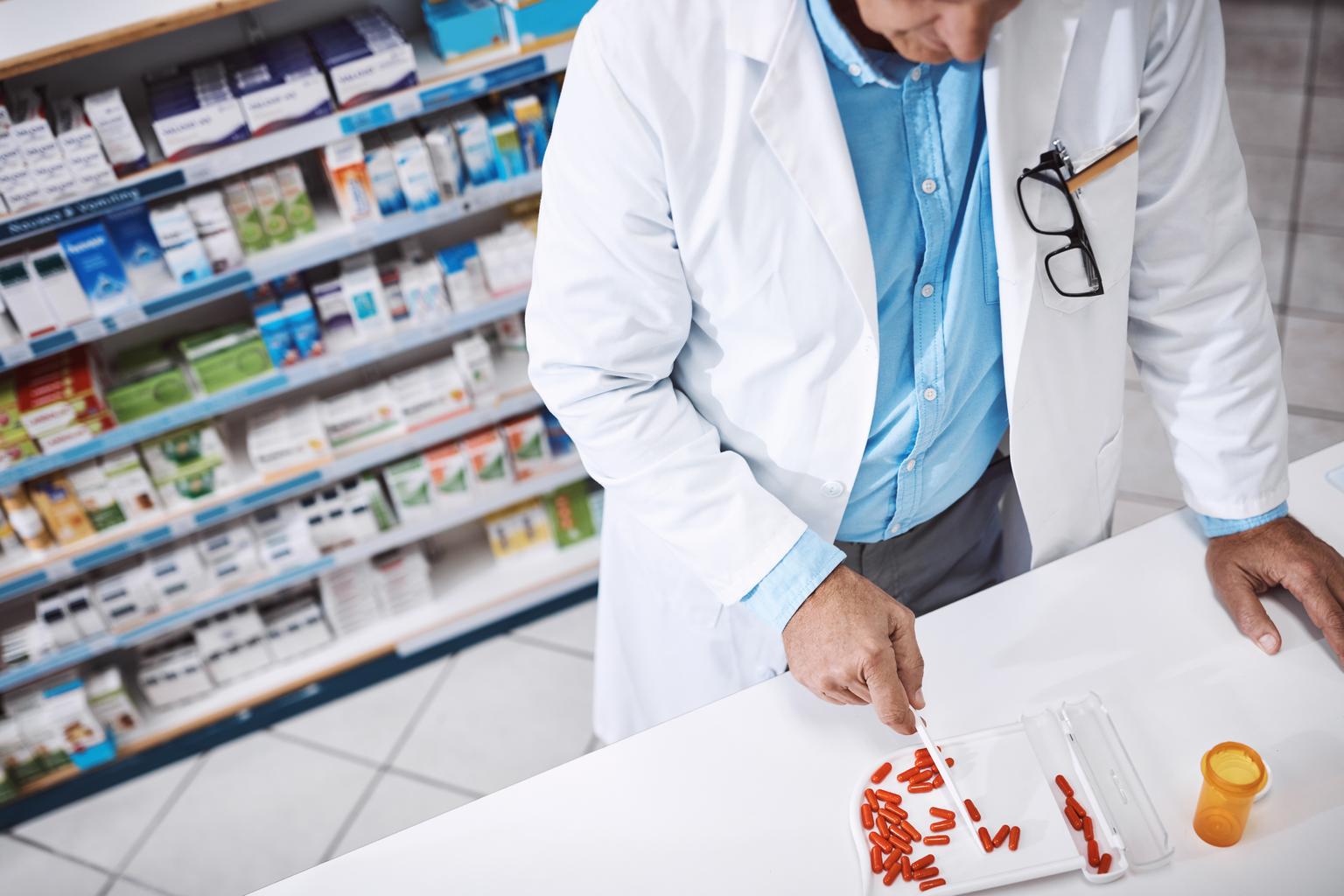 A pharmacist refilling prescription medicine on a counter.
