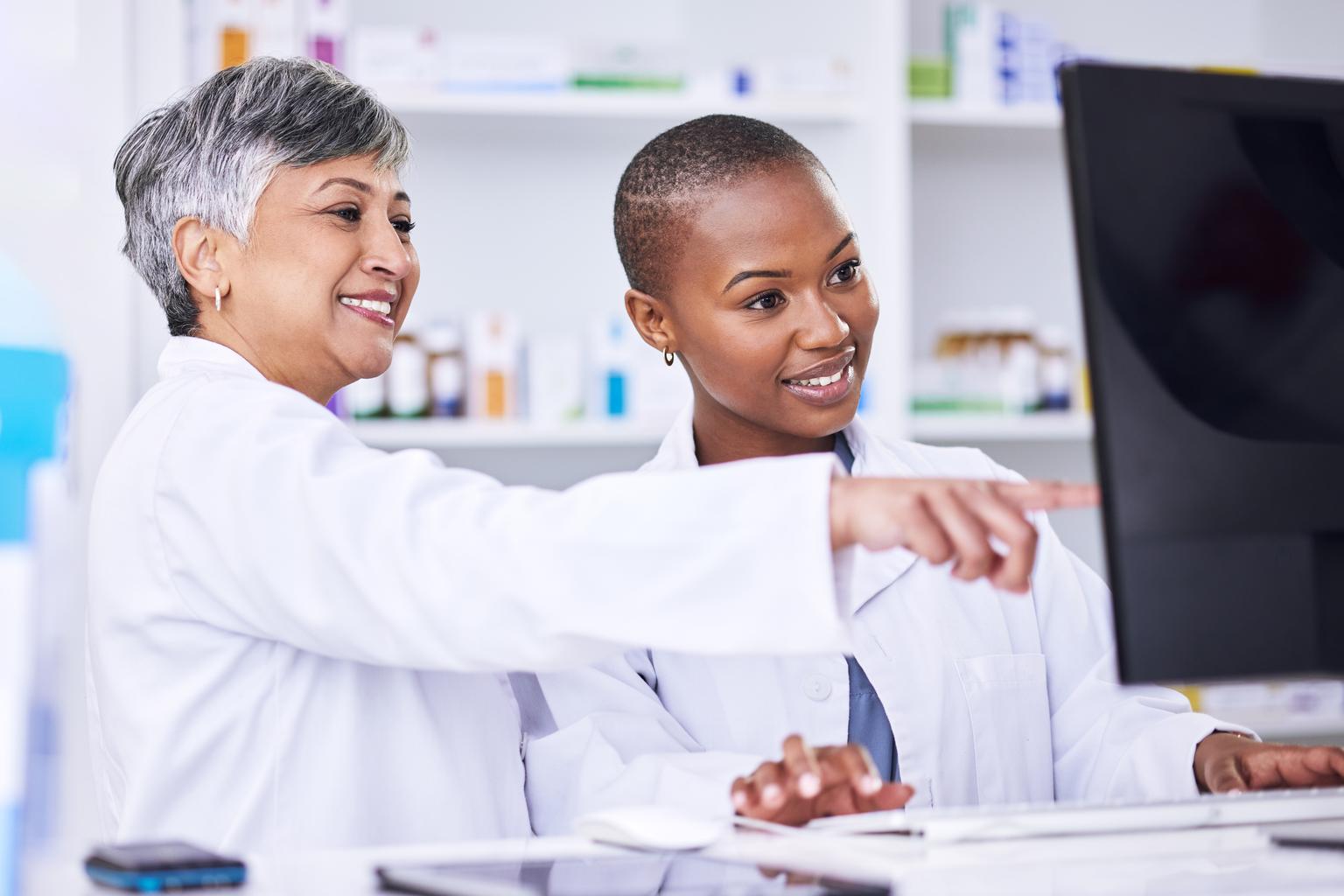 Senior woman pharmacist training female intern on the computer at the pharmacy