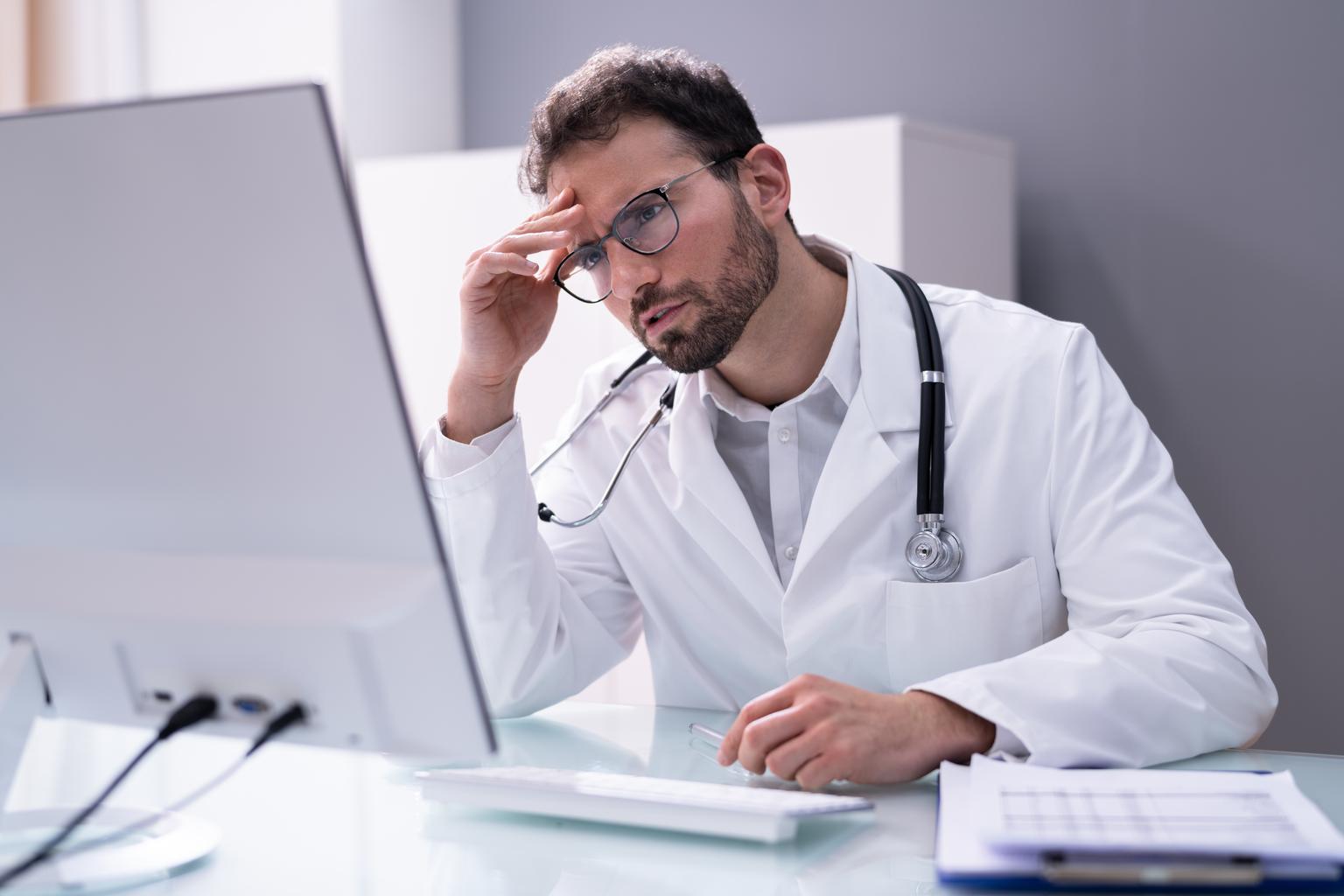 Portrait of a frustrated and overworked male doctor looking at the computer in a hospital GI1318254003