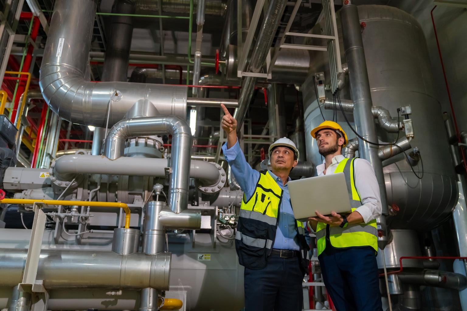 Professional male electrical engineer in safety uniform working and discussion at factory site control room. Industrial technician worker maintenance power system at manufacturing industry plant room.