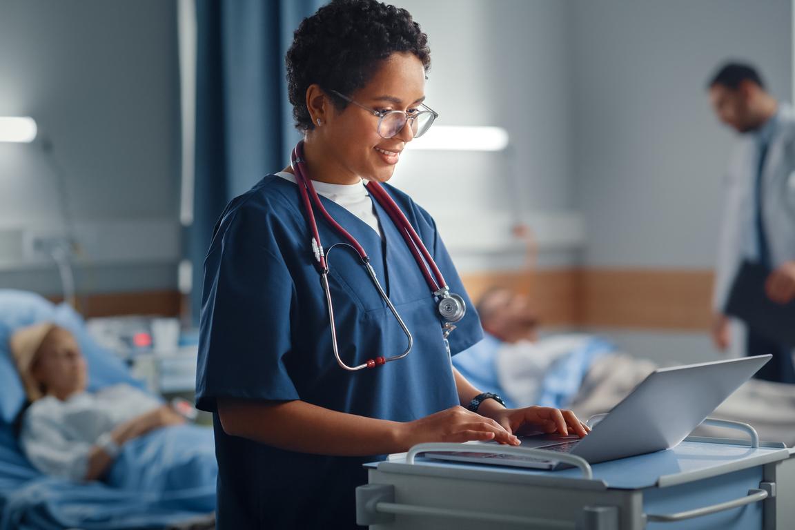 A nurse seen entering patient notes into EHR at patient's bedside.