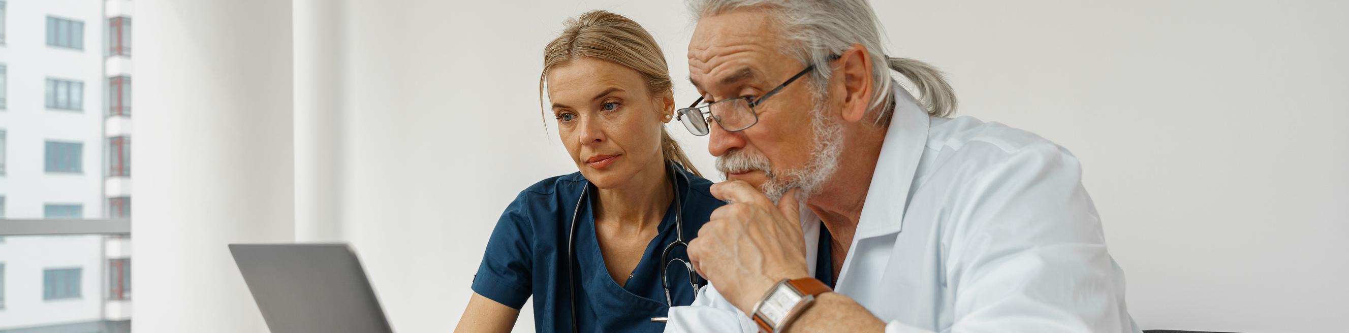 Two doctors discussing patient diagnosis with a laptop sitting in clinic office 